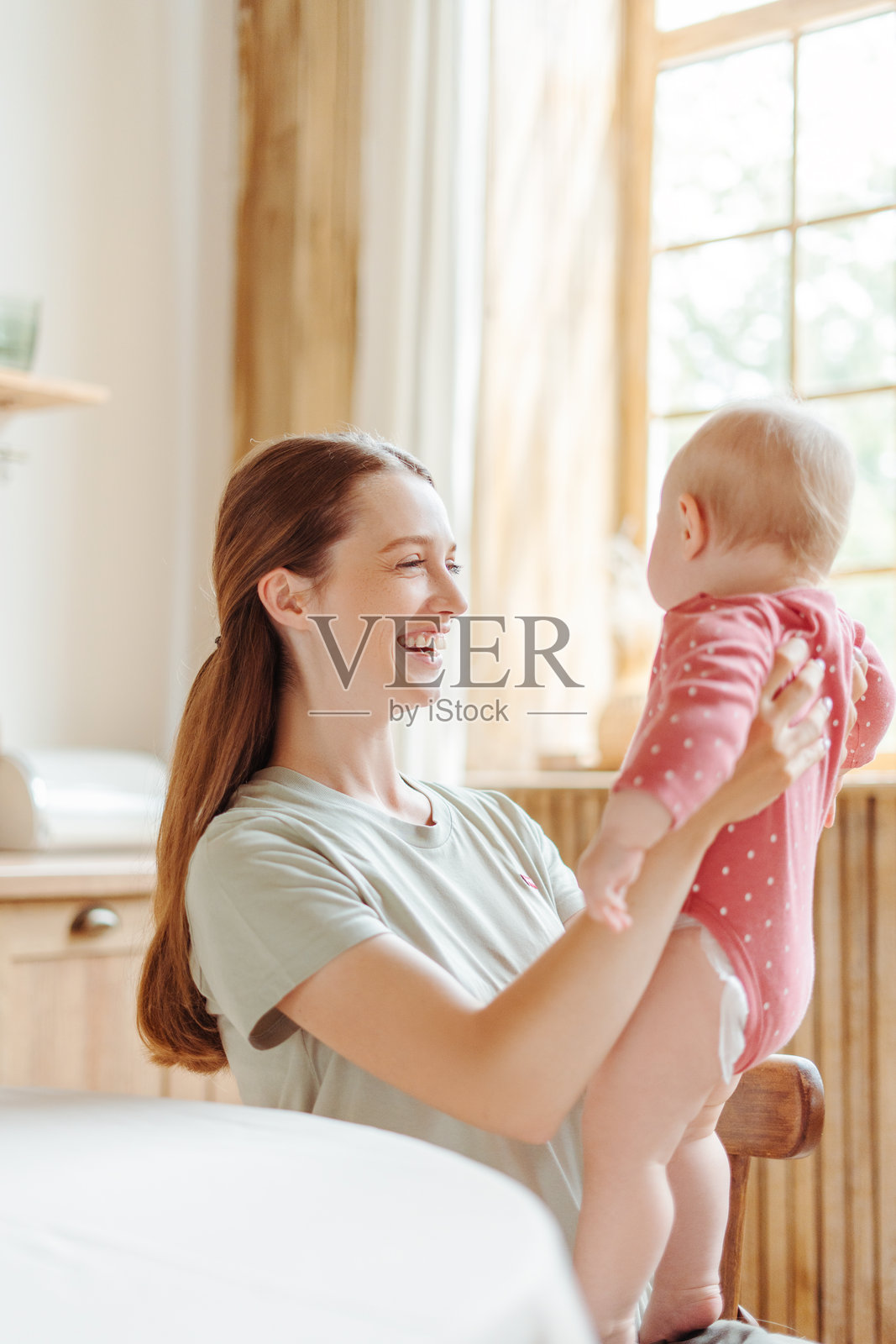 快乐的母亲在家中抱起并举起她的宝宝照片摄影图片