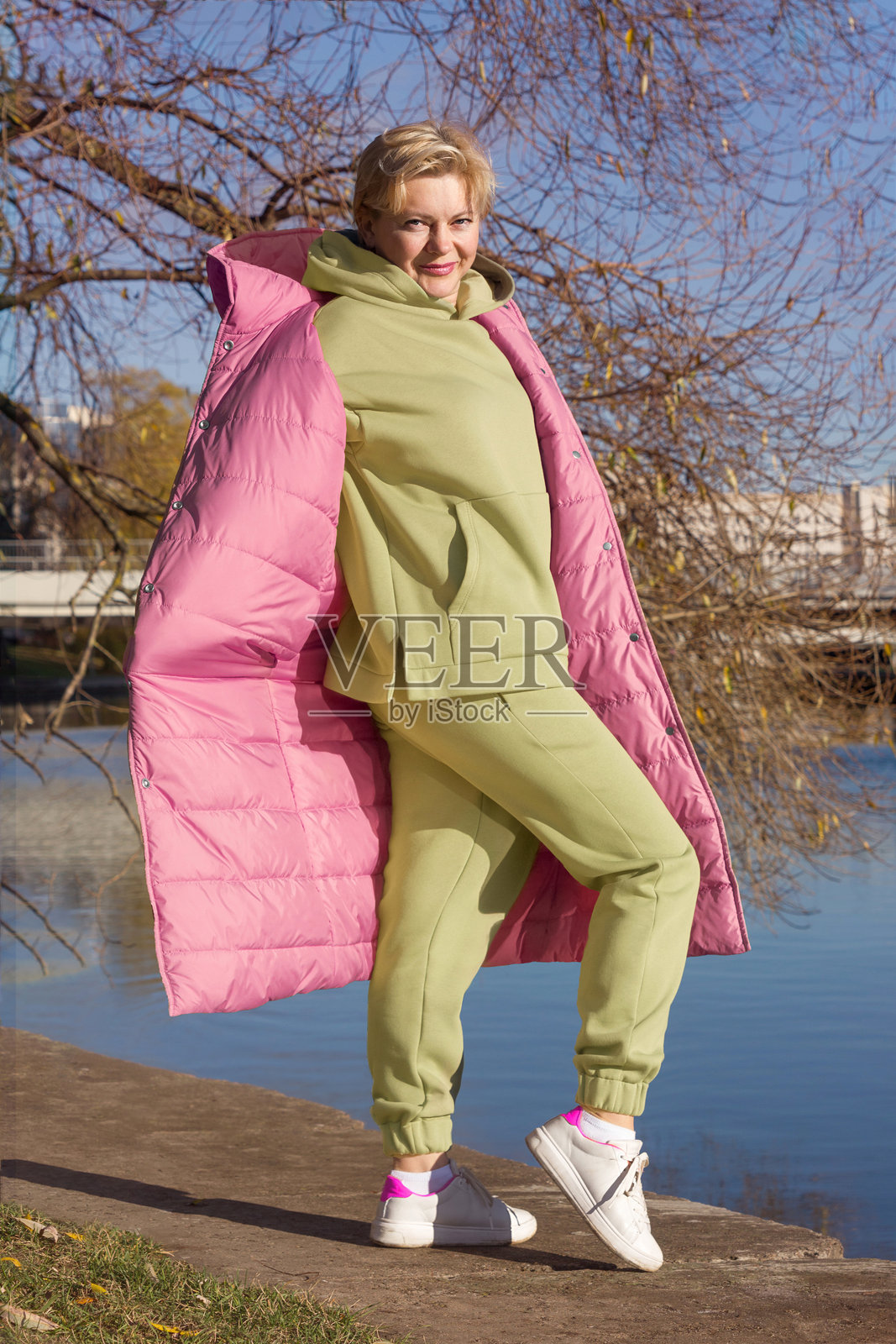 女性穿着绿色连帽衫和长外套在秋季公园散步，时尚。照片摄影图片