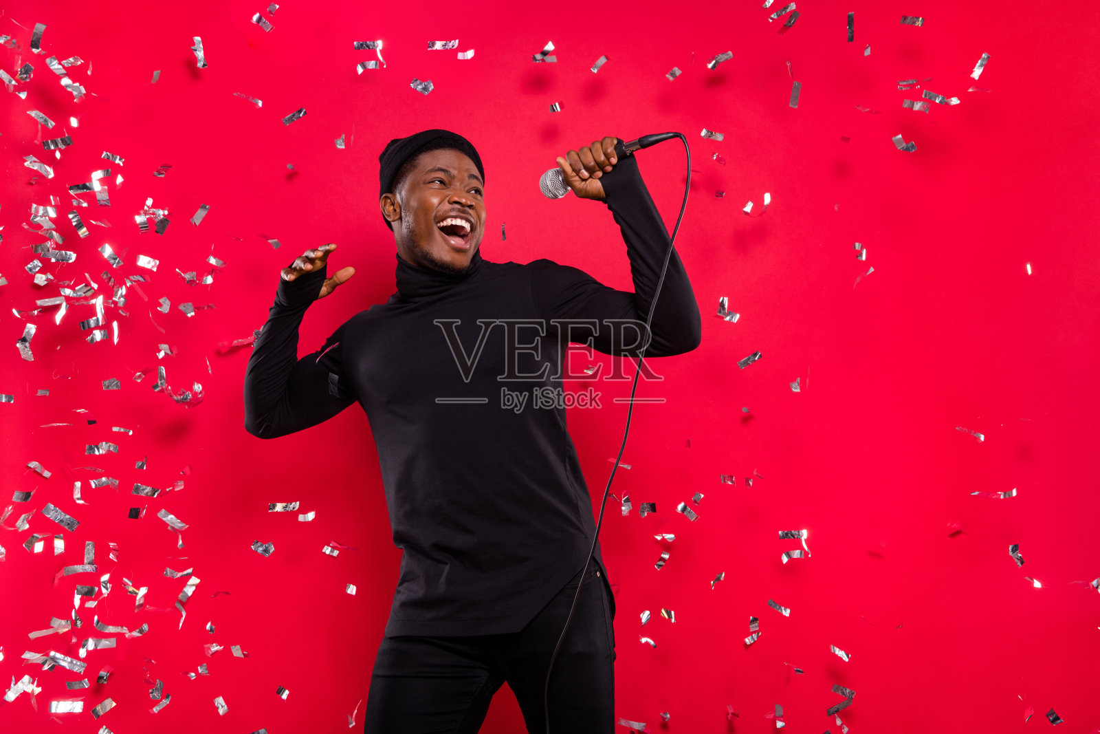 吸引人的快乐男士在明亮的红色背景下唱着热门流行歌曲，心情愉悦，轻松自在。照片摄影图片