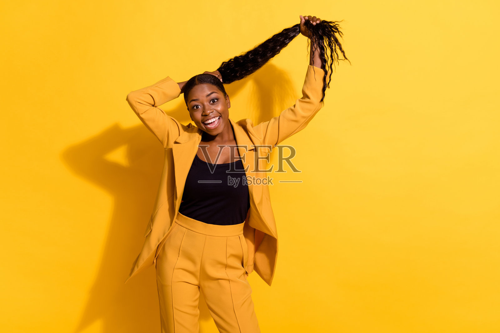 迷人、快乐、时尚的女孩在明亮的黄色背景下扎着马尾，尽情享受乐趣。照片摄影图片