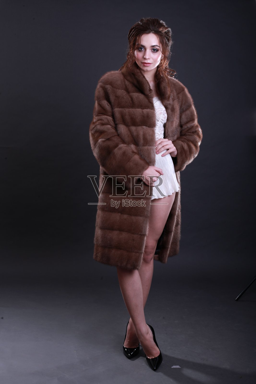时尚年轻女性穿着毛皮外套，站在灰色背景前照片摄影图片