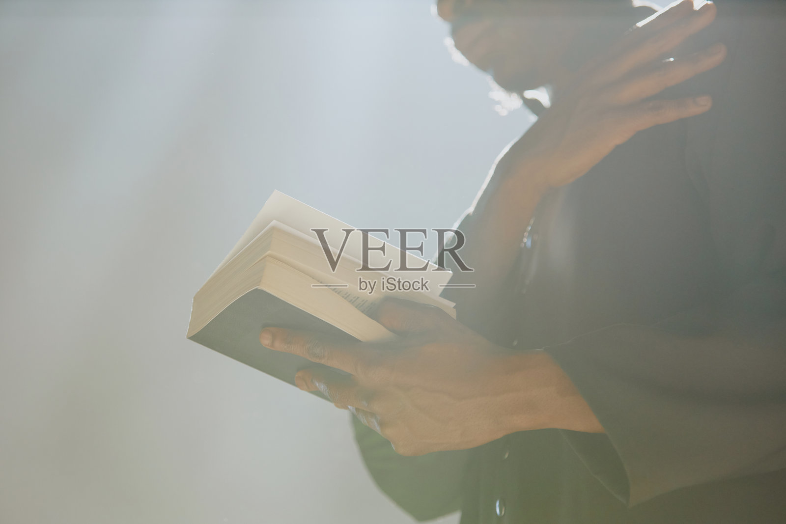 无法辨认的牧师手持圣经为自己划十字。照片摄影图片