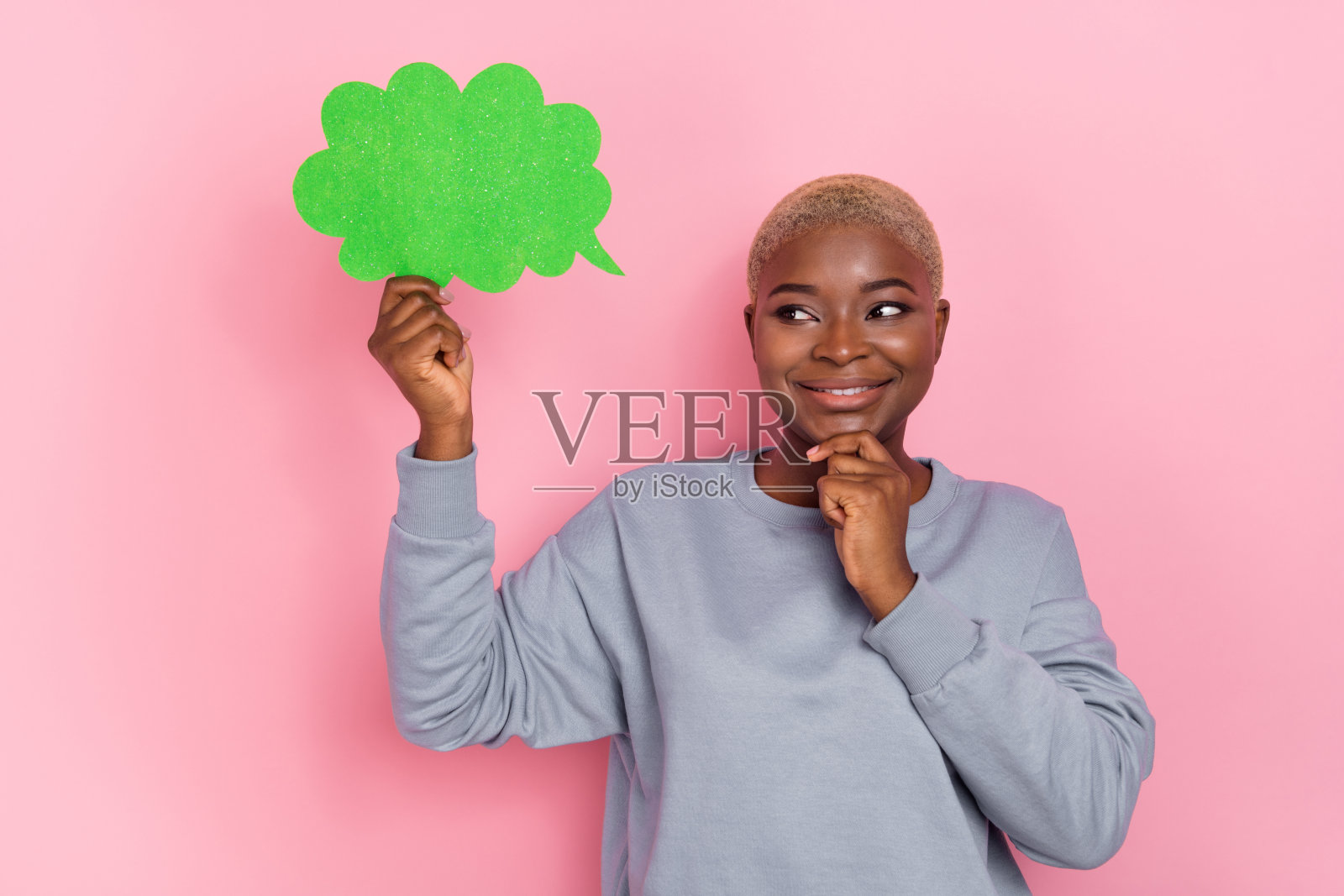 可爱的女孩微笑着，手托着下巴，凝视着空旷的云朵形状卡片，背景为粉色。照片摄影图片