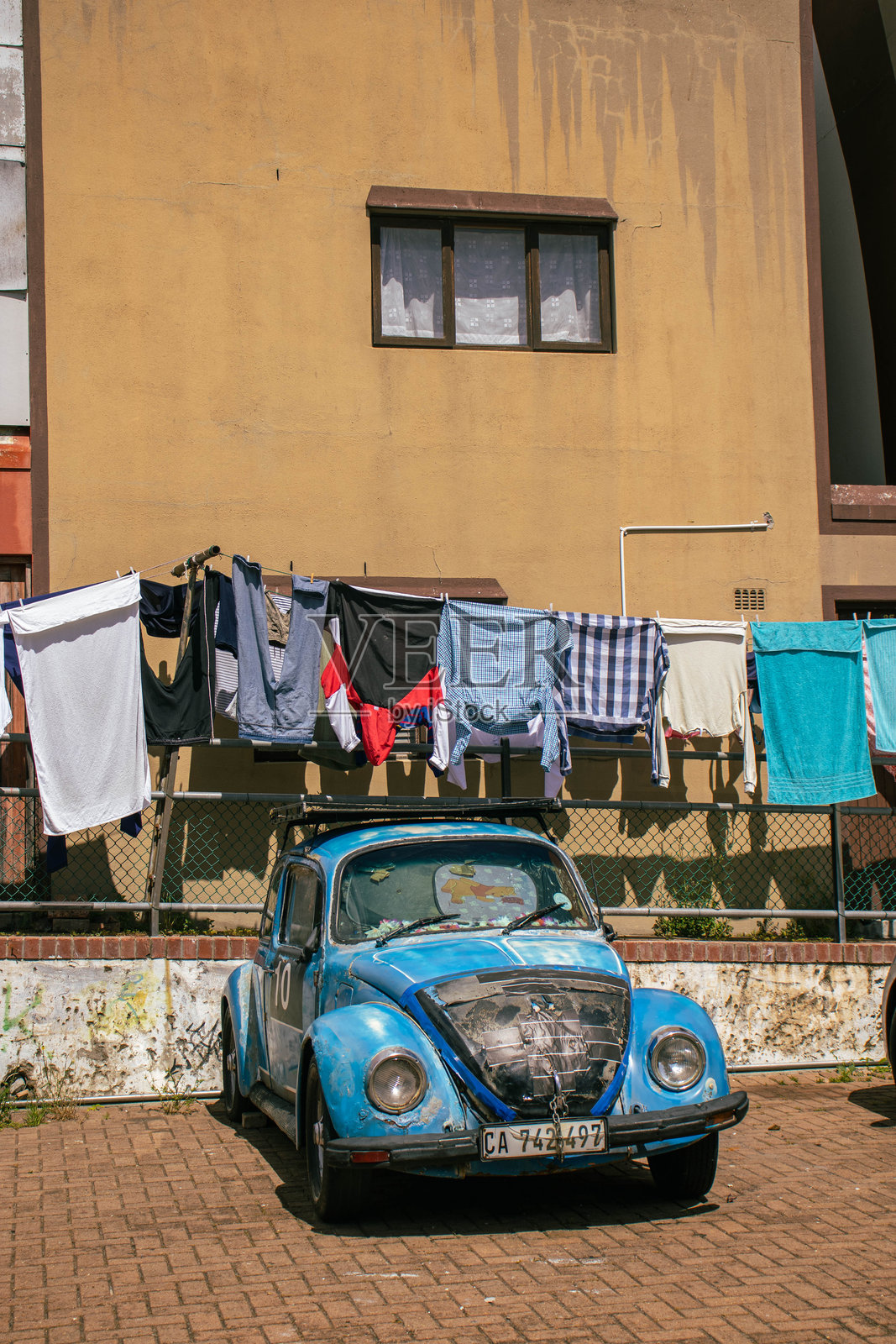 一辆旧甲壳虫汽车停在一栋建筑外,晾衣绳上挂着新鲜的笑脸。照片摄影图片