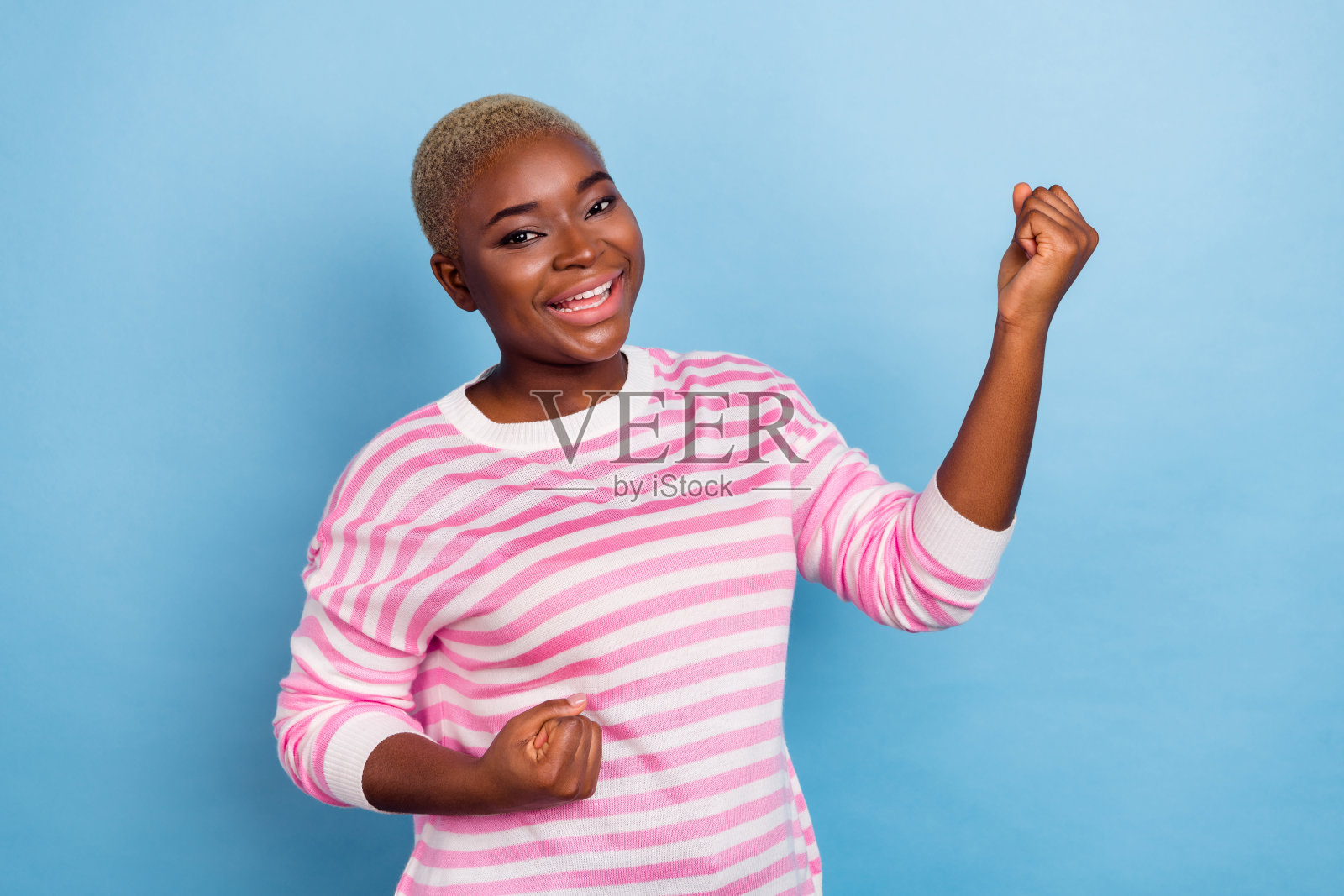 穿着条纹衣服的闪亮兴奋女性举起双臂，享受足球队的成功，背景为蓝色。照片摄影图片