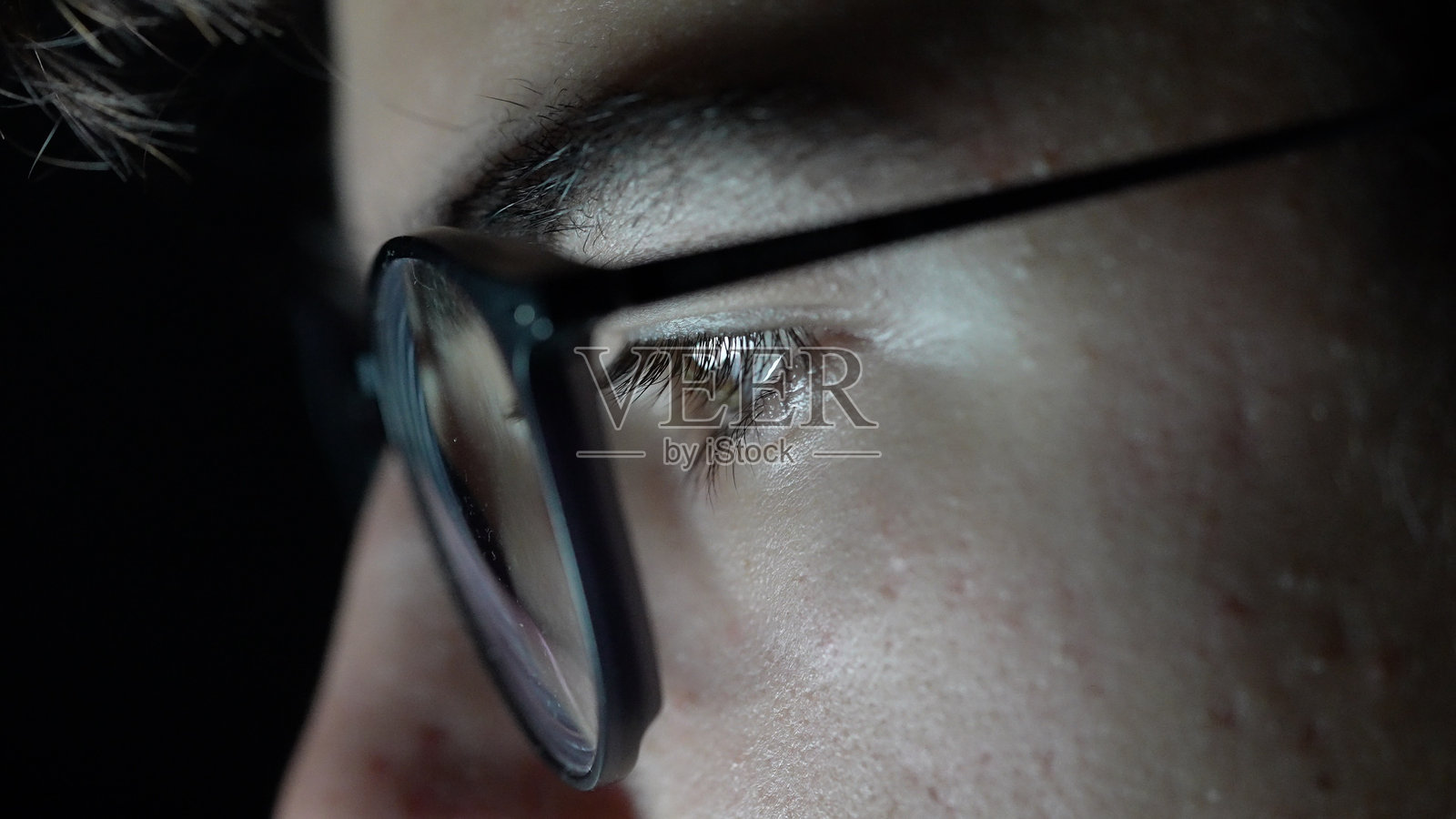 年轻男孩戴着眼镜，近距离特写他的眼睛，面前是黑色背景的笔记本电脑。照片摄影图片