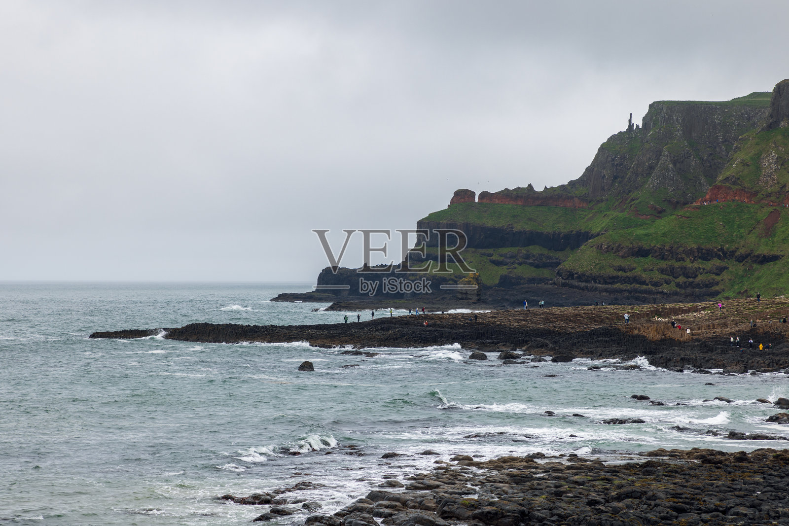 北爱尔兰的巨人之路，游客们在欣赏著名的玄武岩柱和大西洋边的崎岖悬崖。照片摄影图片