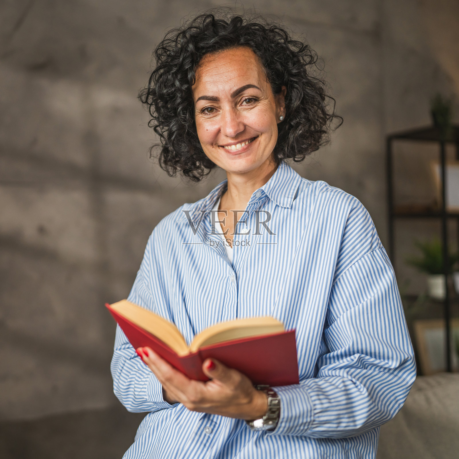 美丽的成熟的女性在灰色墙前阅读一本书照片摄影图片