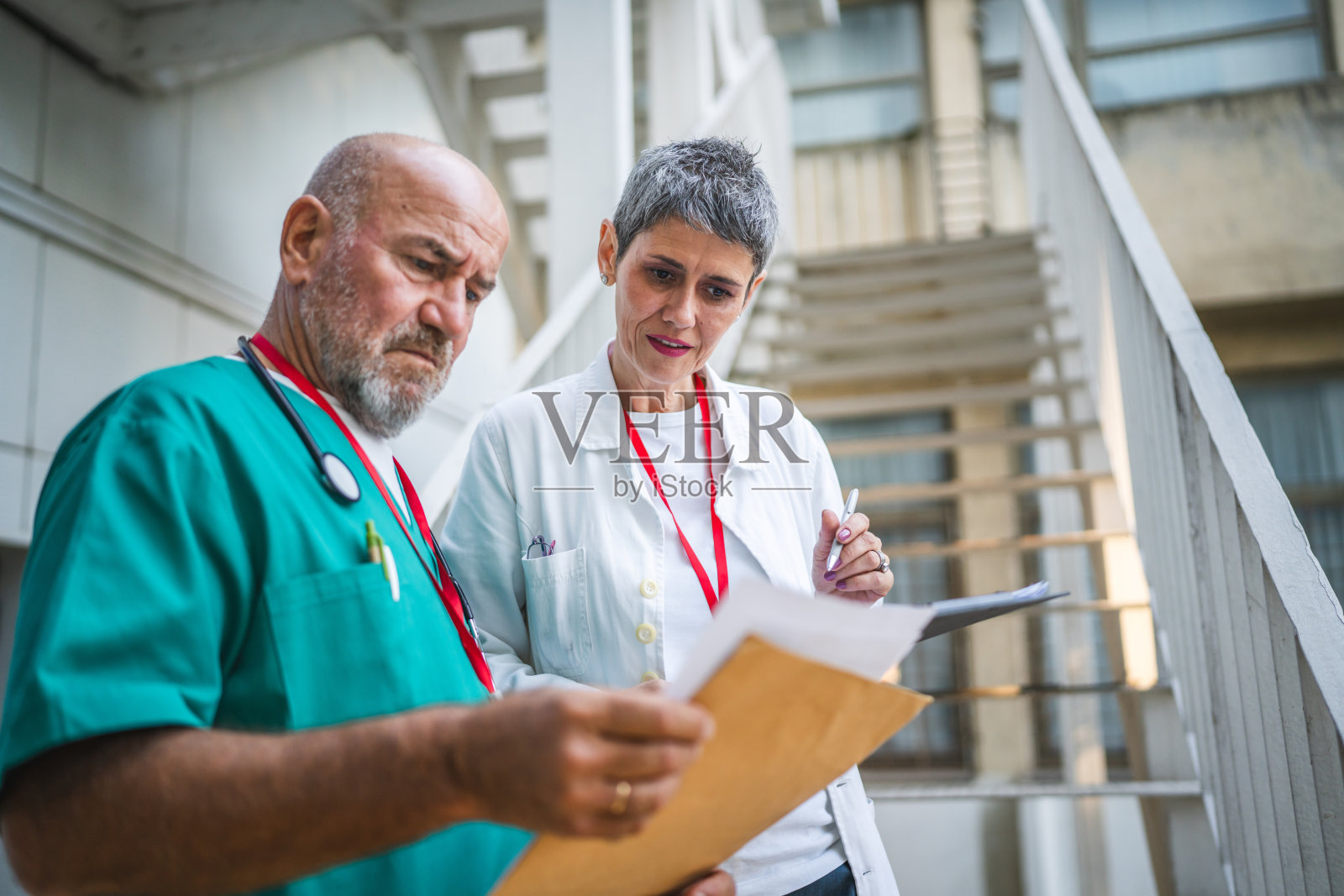 两位医生在楼梯上查看夹板上的信息并记录。照片摄影图片