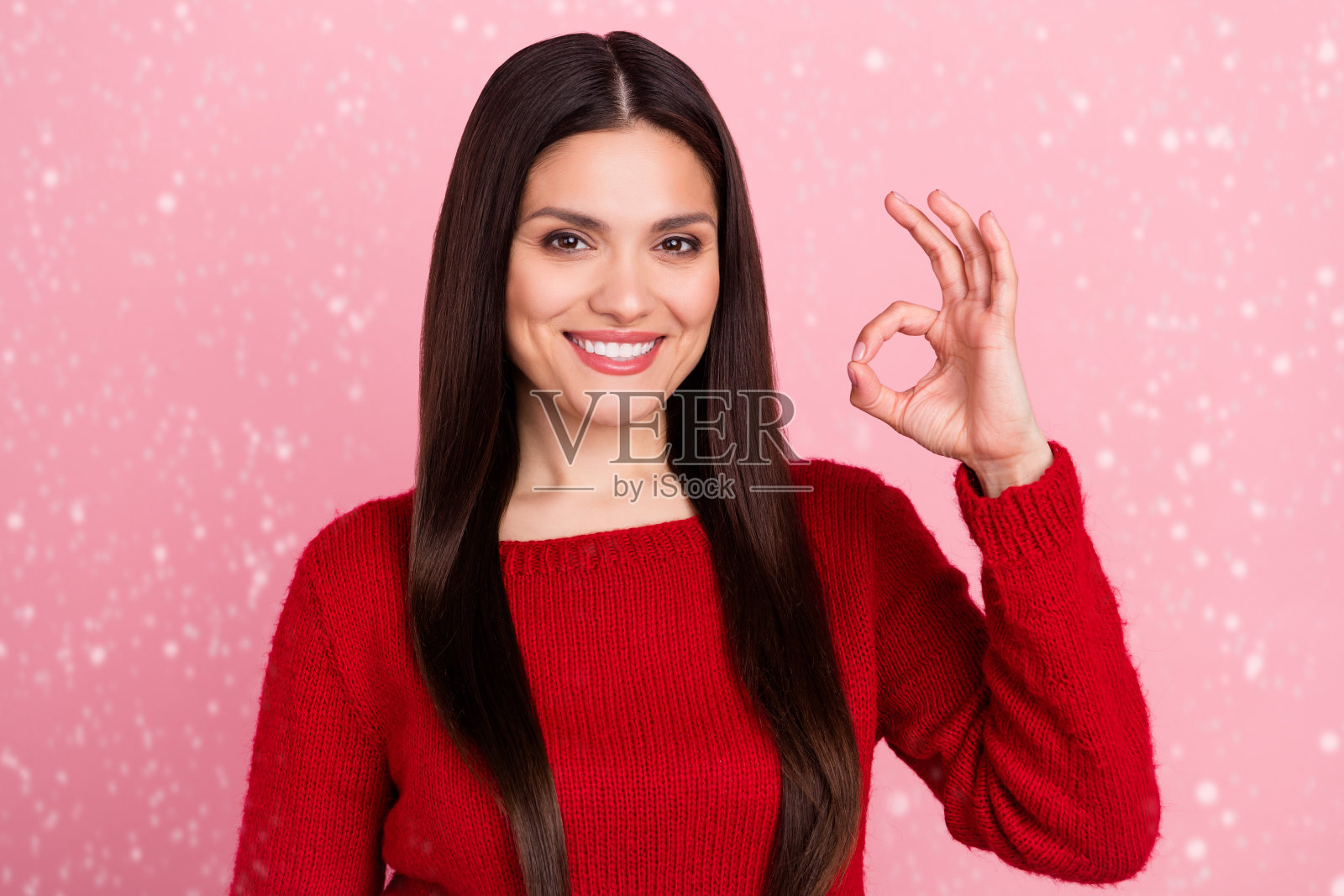 乐观的棕发女士在粉色背景下穿着红色毛衣做出“好”的手势照片摄影图片