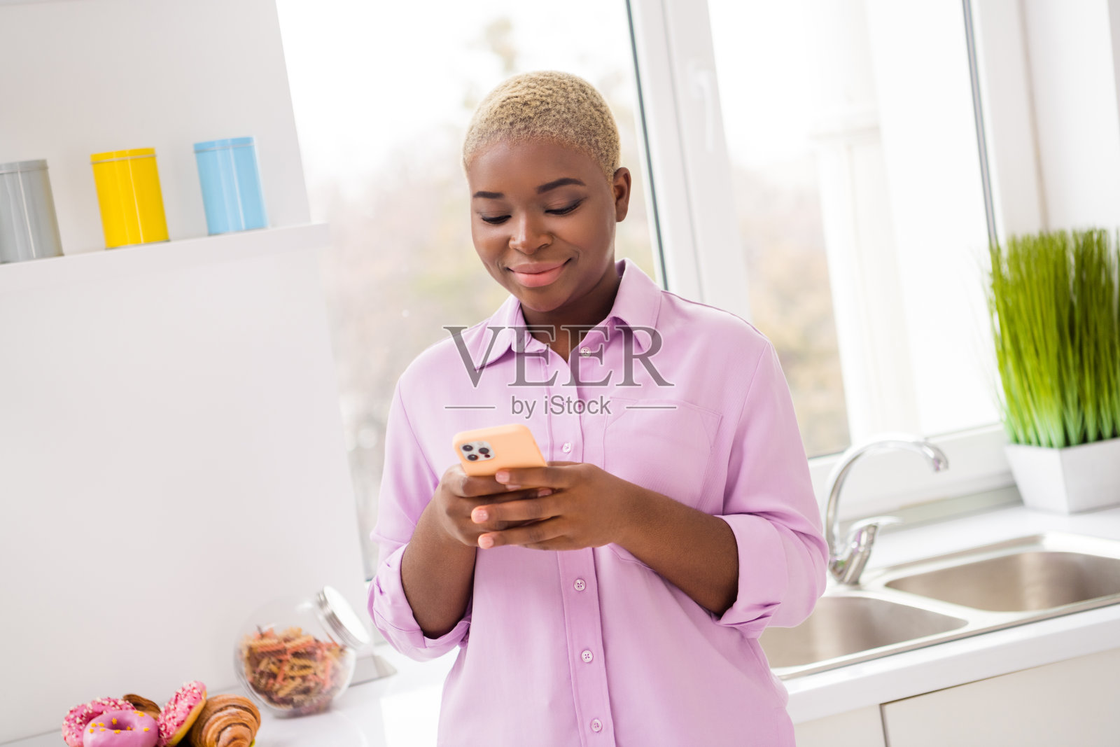 安静满足的女士在室内厨房里使用电话，撰写博客文章并聊天。照片摄影图片