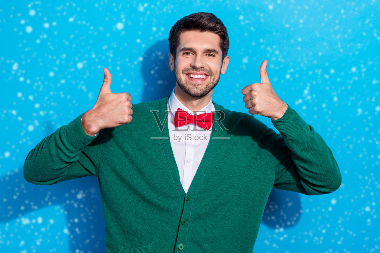 快乐的帅气男士双手竖起大拇指，满意地享受新季购物假日娱乐，背景为蓝色。照片摄影图片