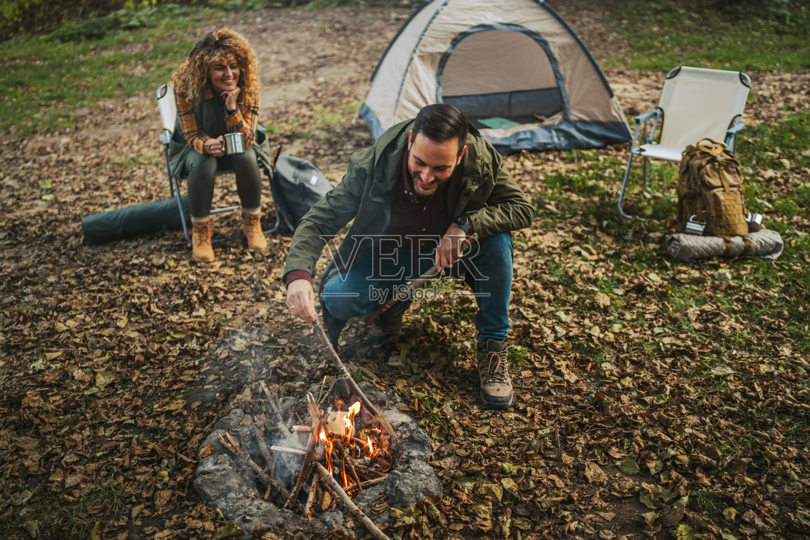 成年男性徒步旅行者跪下用木材生火，为露营做准备照片摄影图片