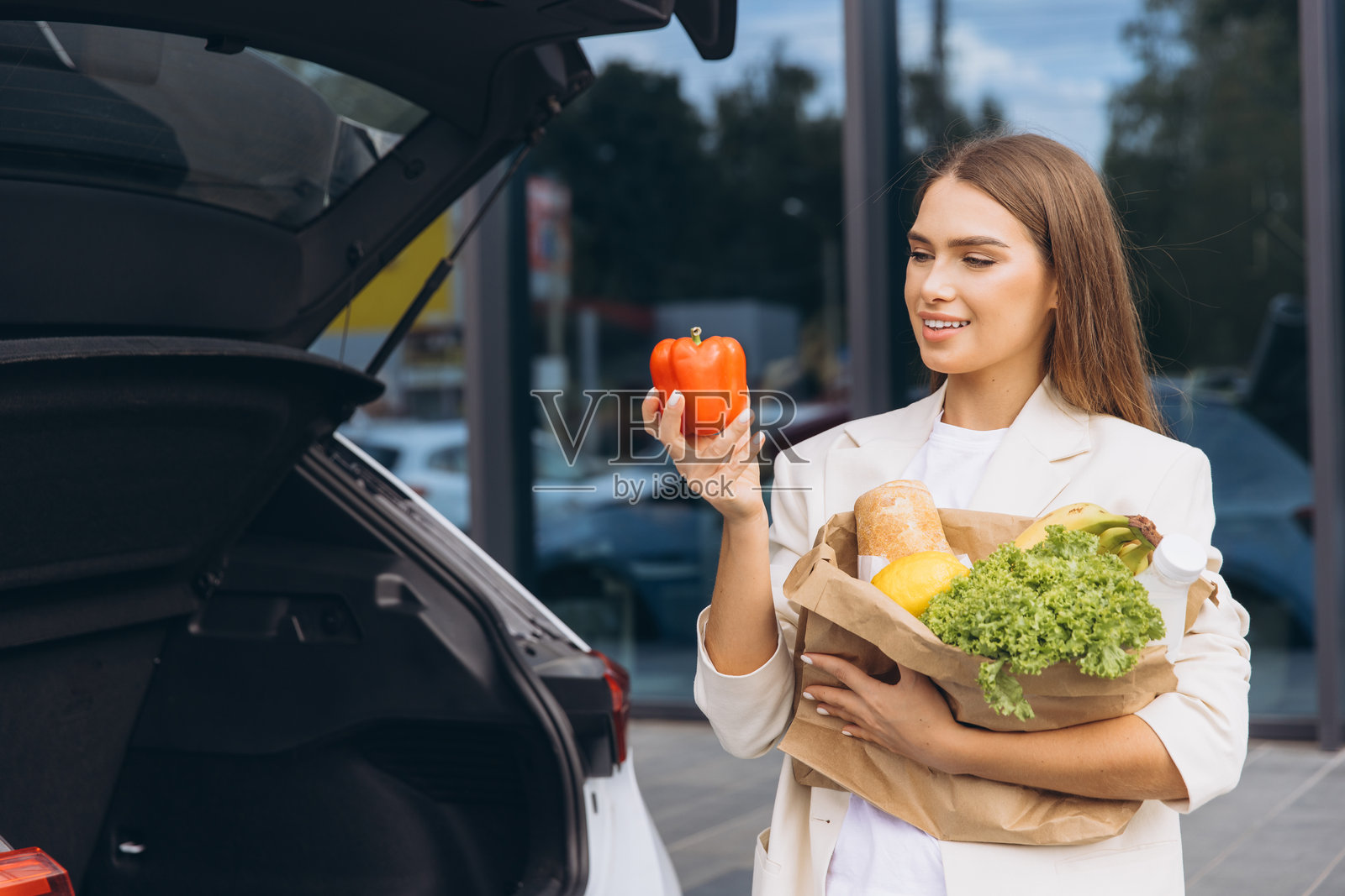 女人在车旁拿着装有新鲜蔬菜和面包的购物袋照片摄影图片