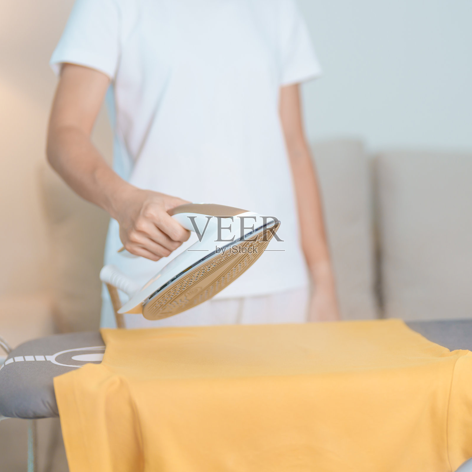 女性在熨衣板上使用电熨斗熨烫T恤，智能自动蒸汽熨斗。洗衣、家务、家庭清洁、家庭卫生、日常琐事和日常生活概念。照片摄影图片