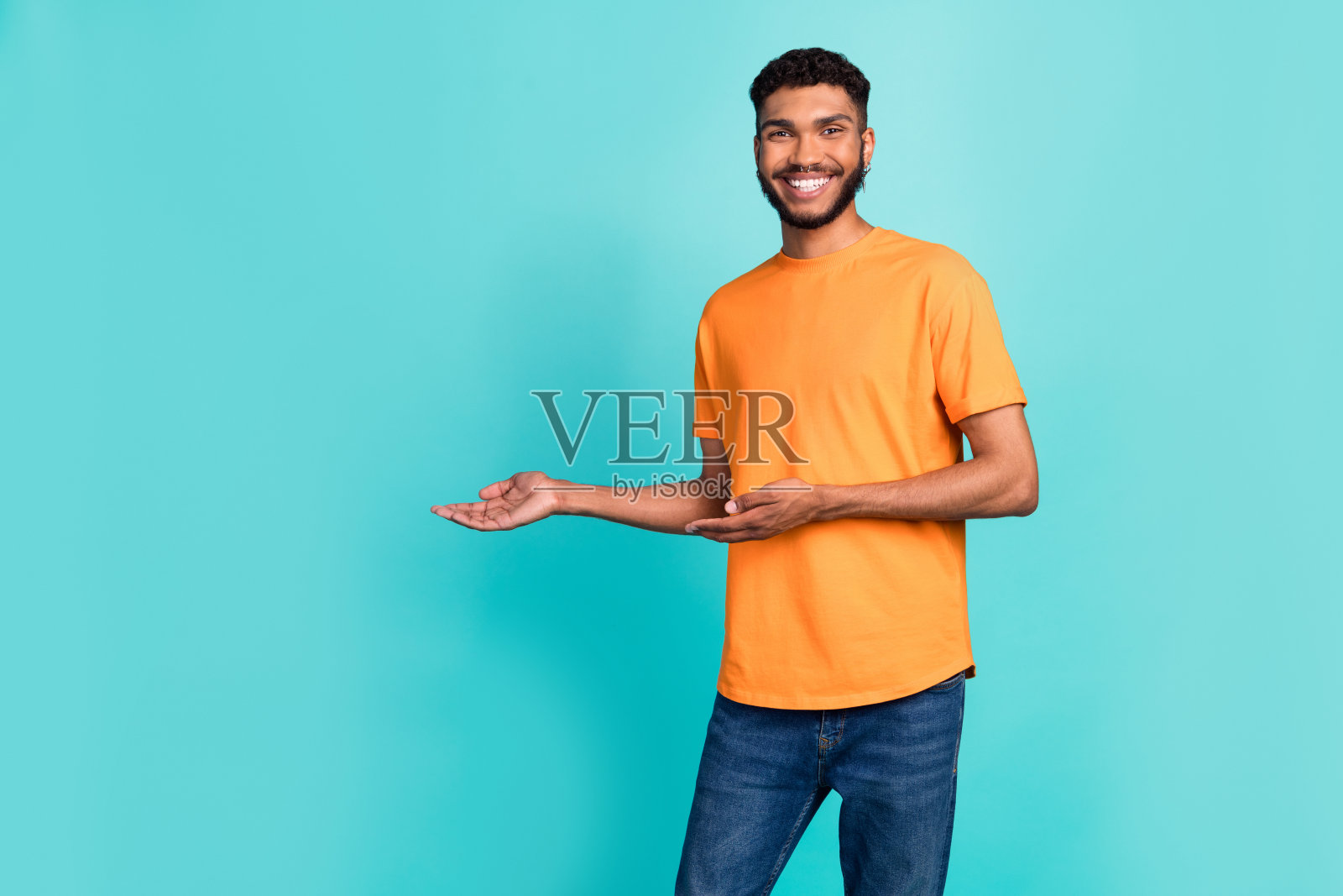 穿着橙色T恤的积极阳光男孩微笑着，双臂张开，仿佛在拥抱空旷的空间，背景为青色。照片摄影图片