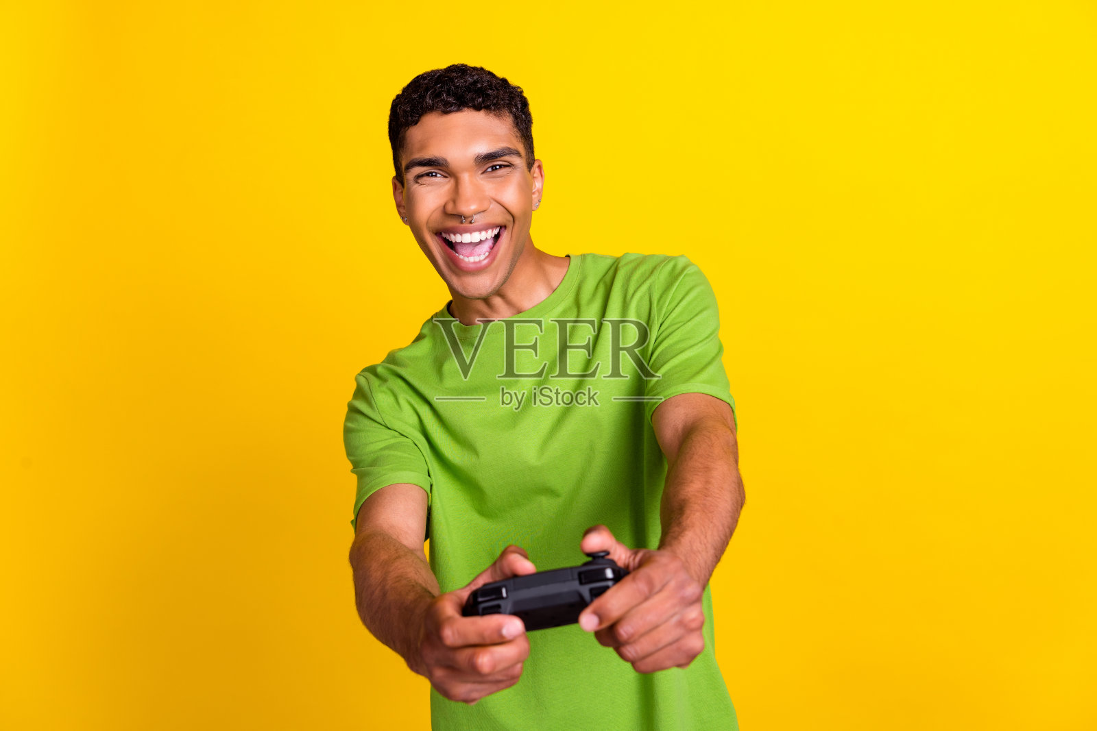 年轻帅气男孩穿着绿色T恤，在黄色背景下休闲时光玩游戏手柄。照片摄影图片