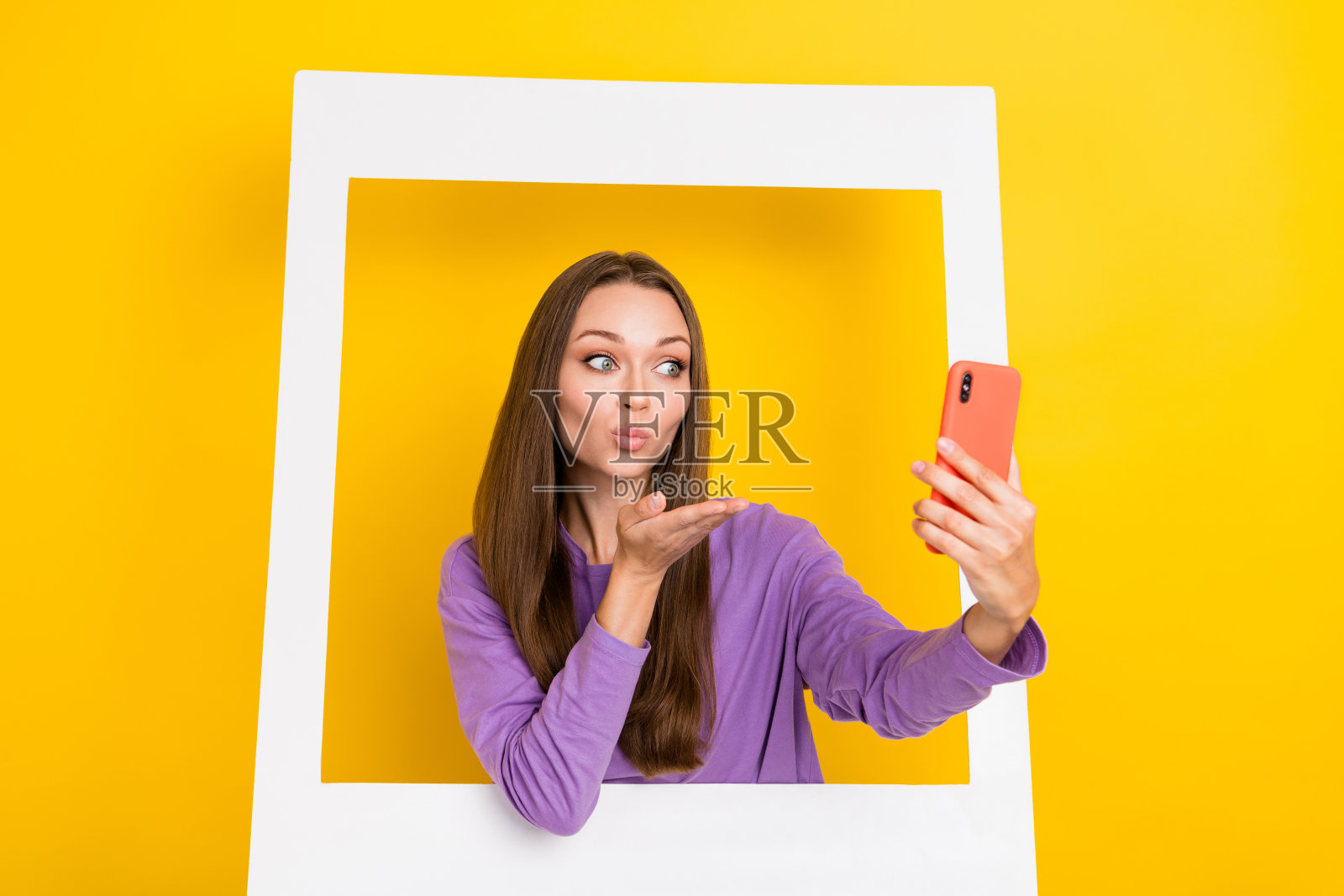 年轻兴奋的女性特写肖像，拍摄自拍照，送出空气吻，框架名人，背景为明亮的黄色。照片摄影图片