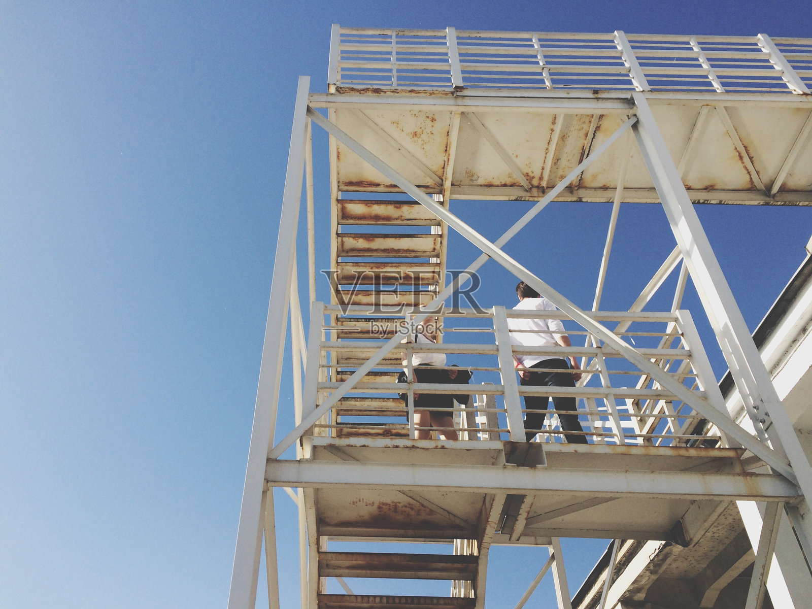 低角度视角下的男女站在金属桥上，背景是天空照片摄影图片