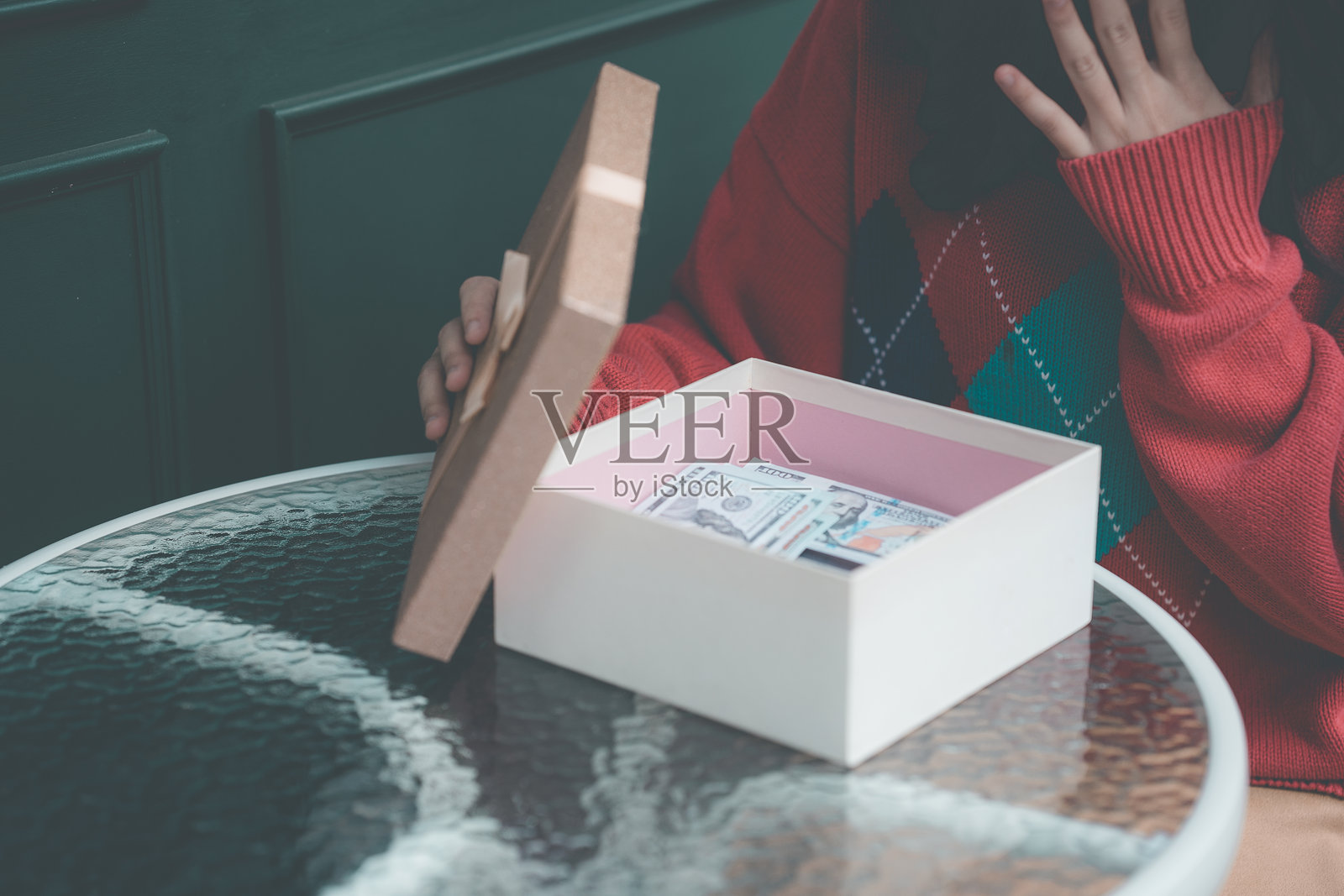 年轻的亚洲女性戴着红白相间的圣诞帽，身边围绕着礼物盒，手中拿着一个红色的圣诞礼物。传递出酷炫、积极和快乐的新年气氛。照片摄影图片