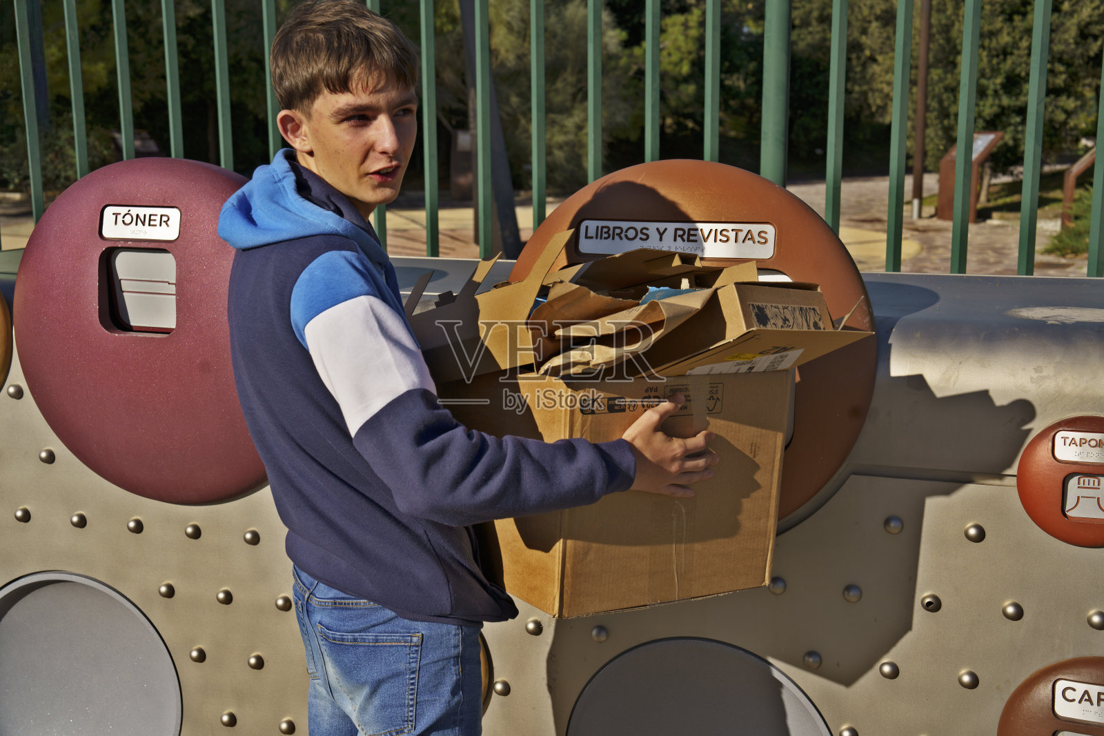 一个年轻男子正在拿着一个纸箱并将其放入垃圾桶。照片摄影图片