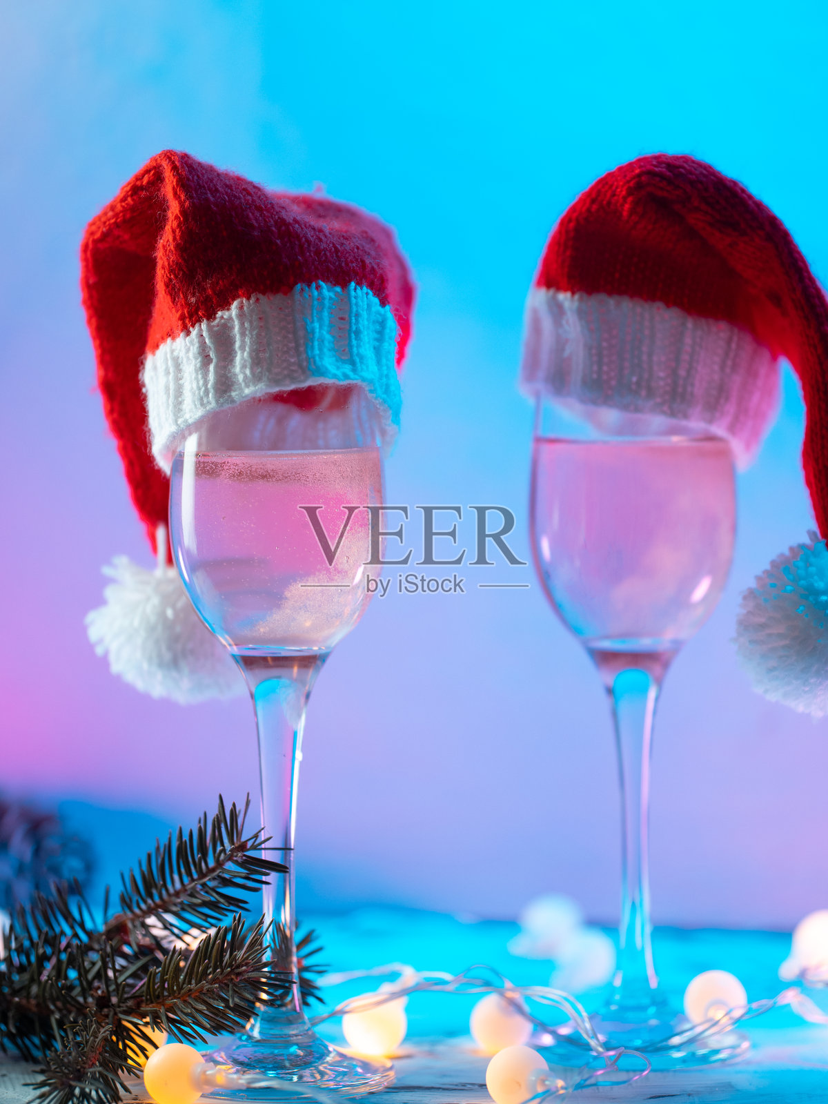 圣诞香槟，两杯戴着圣诞老人帽子的酒杯。节日灯光，霓虹背景照片摄影图片