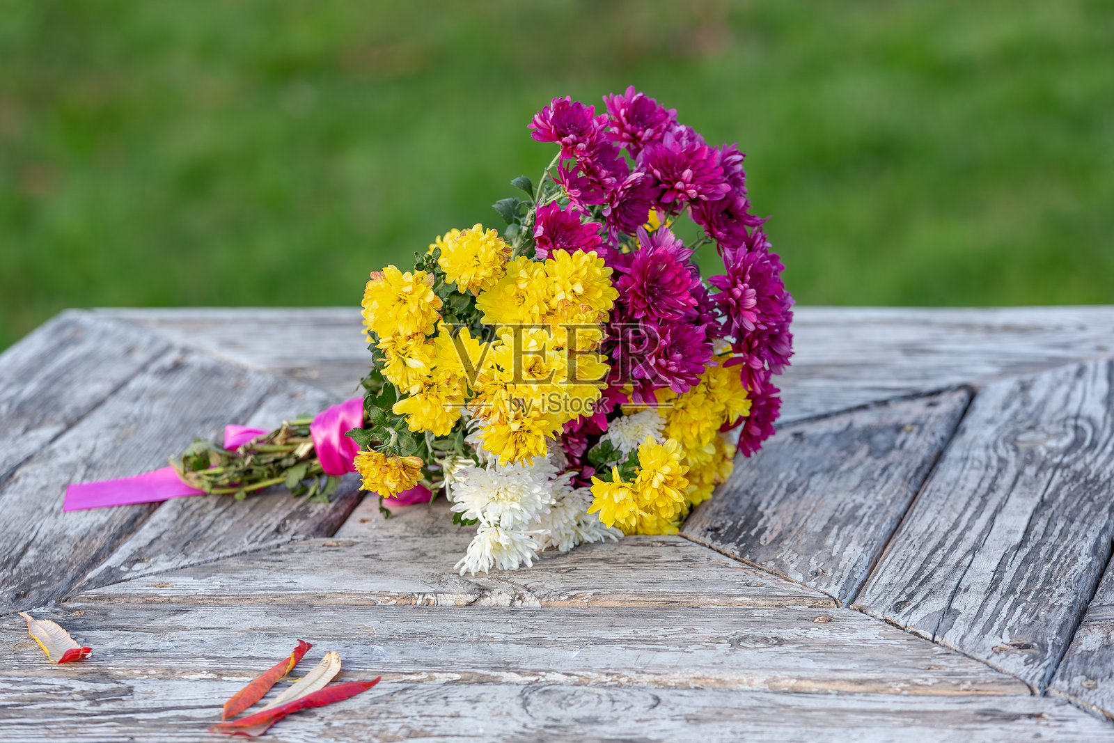 一束花放在乡村风格的木桌上。色彩斑斓的黄色、粉色和白色花朵用粉色丝带包裹，静静地躺在一张风化的木桌上。照片摄影图片