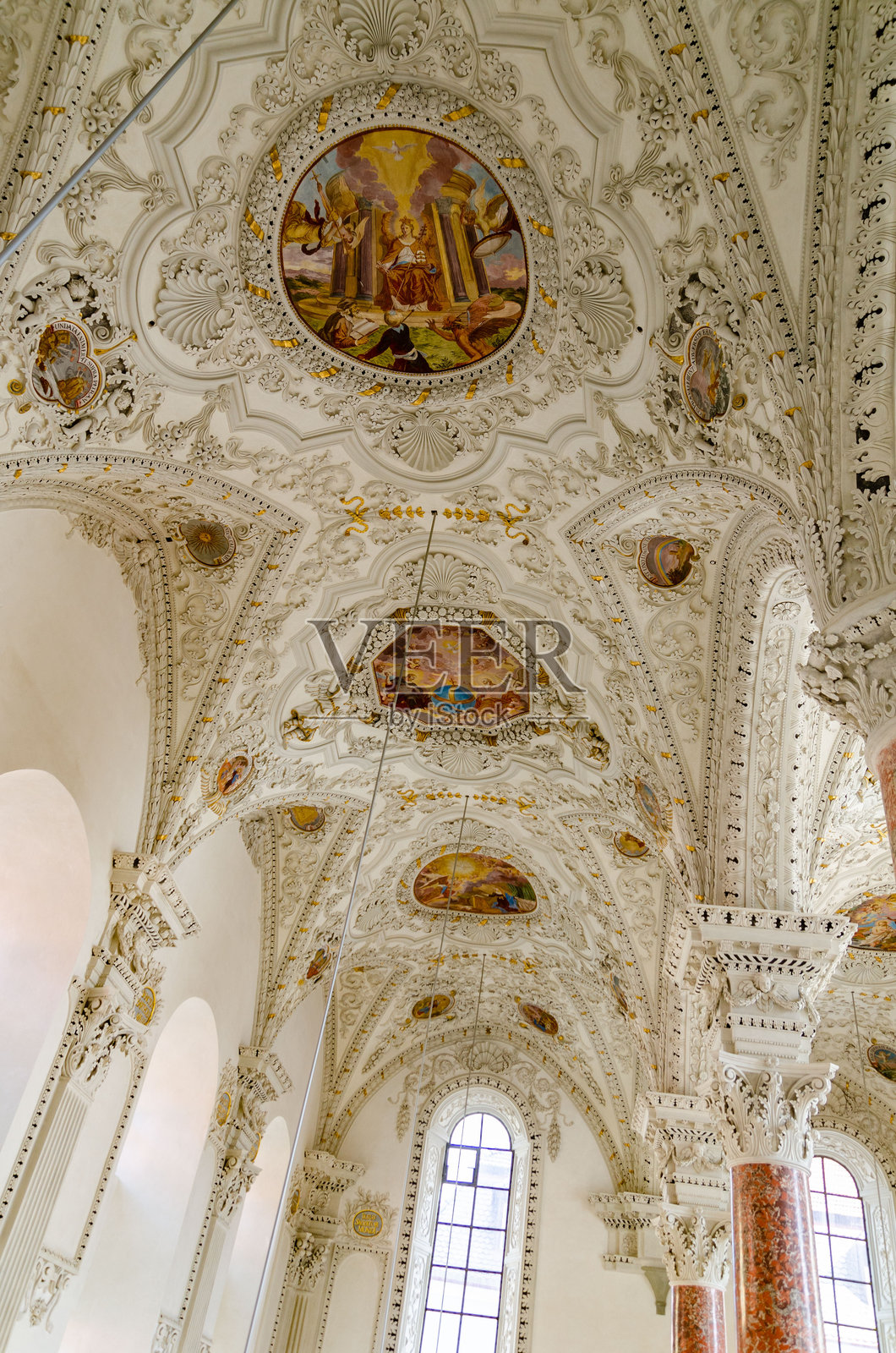 巴洛克风格教堂的内部，装饰华丽的拱形天花板上绘有描绘宗教场景和符号的壁画和雕塑，顶部有高拱窗户透入光线。照片摄影图片
