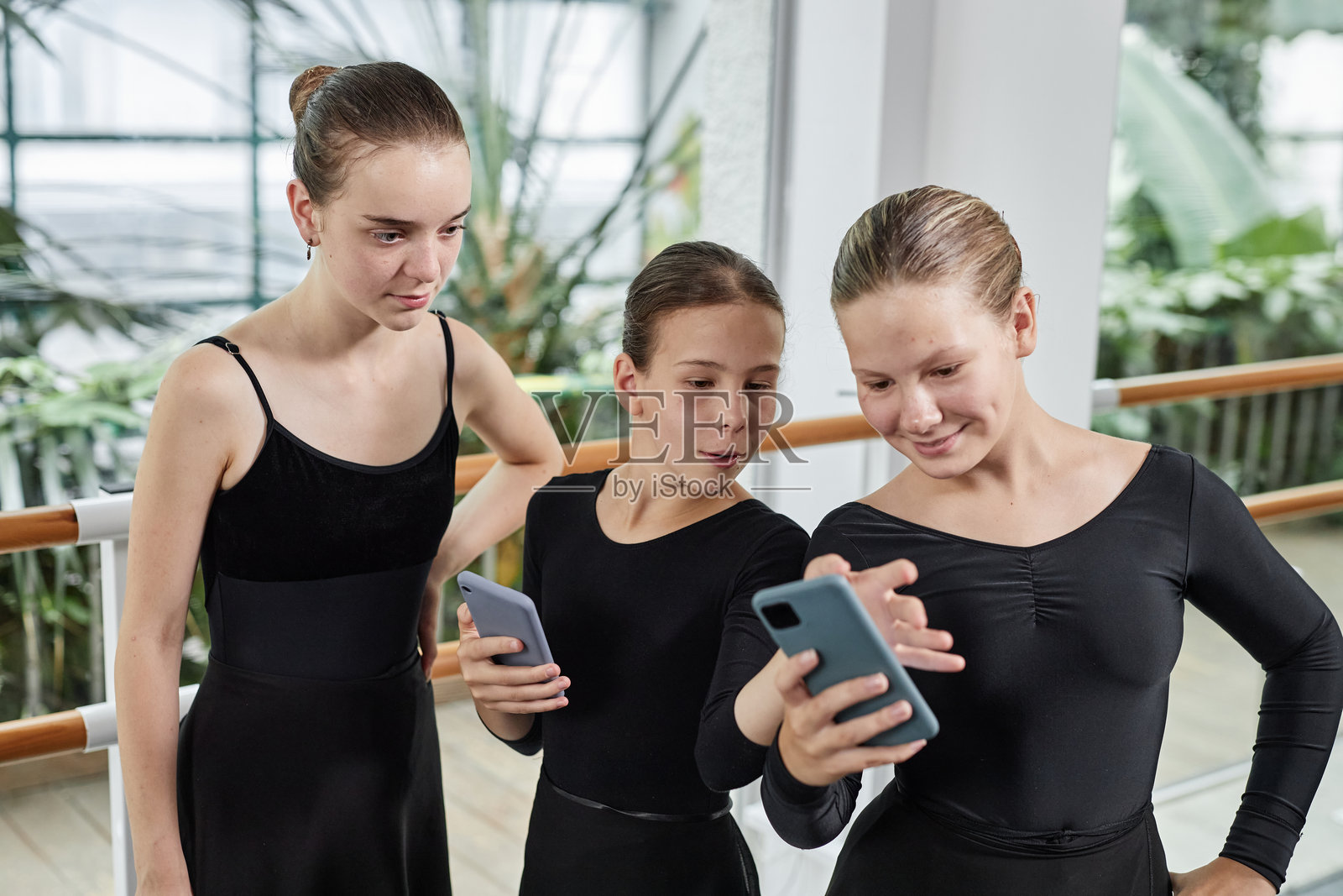 三位芭蕾舞者在室内锻炼后玩手机，享受快乐时光照片摄影图片