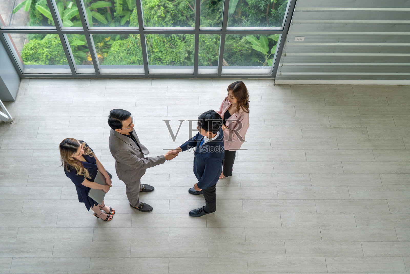 现代办公室中，商业伙伴握手。站在窗边，阳光洒在他们身上。照片摄影图片