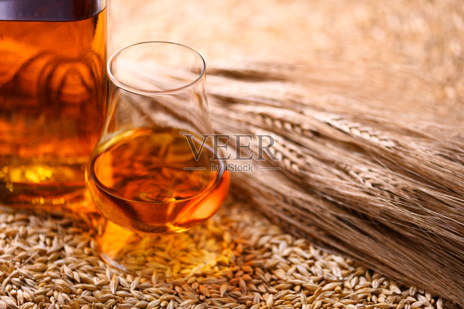 一杯威士忌与瓶子放在大麦粒上照片摄影图片