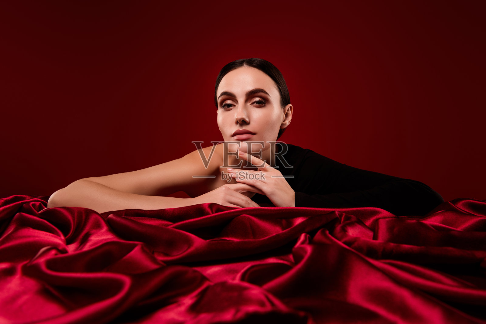美丽的女孩躺在红色柔软的天鹅绒织物上，背景色彩鲜艳。照片摄影图片