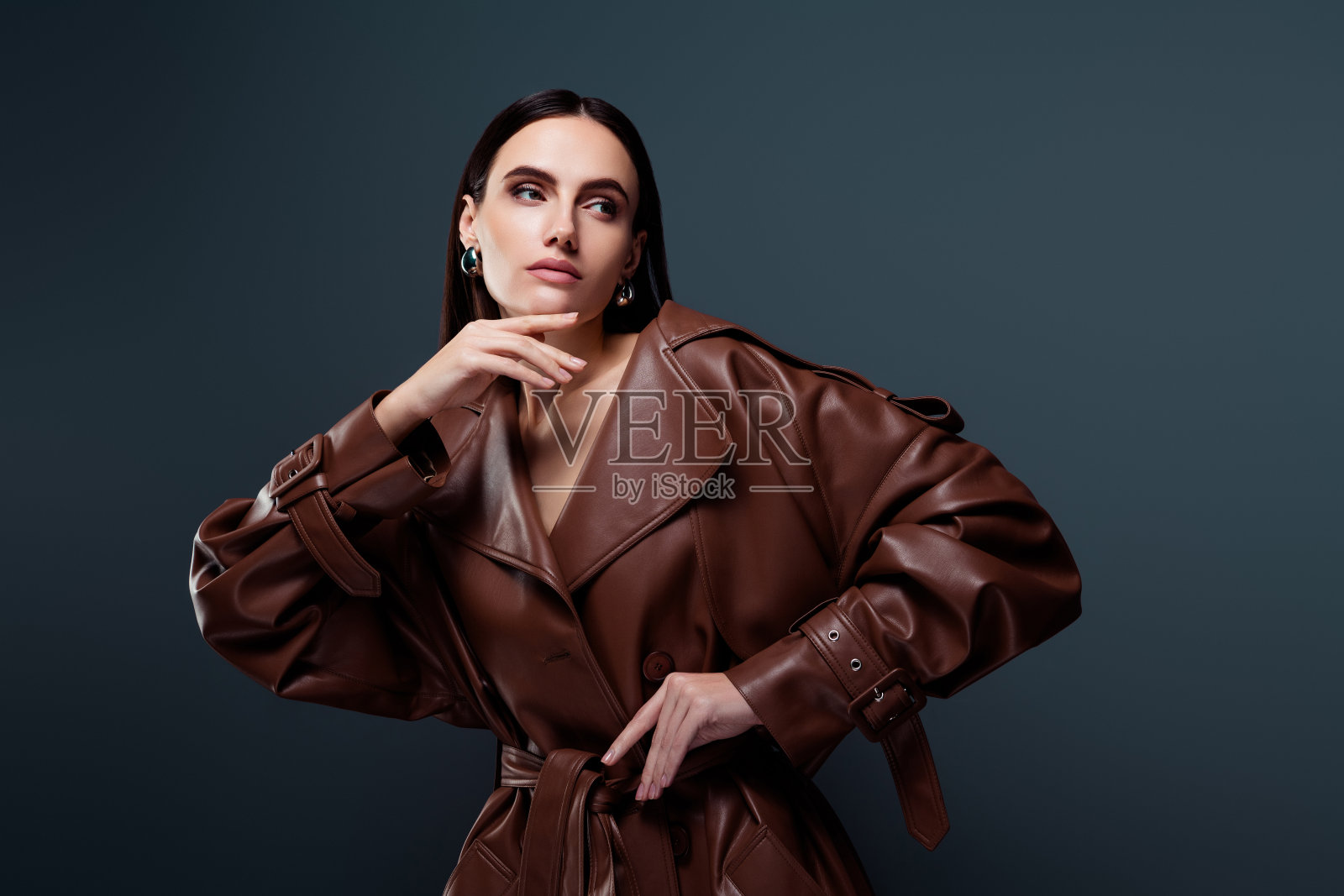 时尚迷人的女士穿着时髦的酒红色皮革雨衣，独自摆姿势，背景为深灰色。照片摄影图片