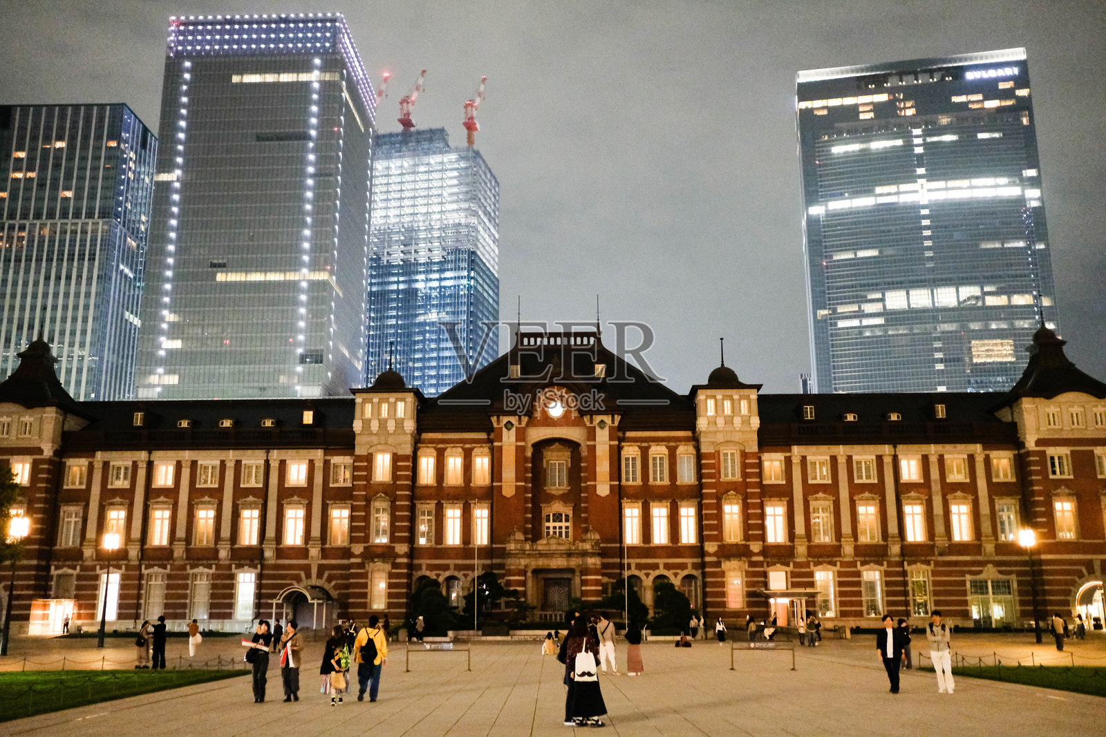 东京车站，东京，日本 - 夜晚灯光下的东京铁路车站外观，广场上有许多人。照片摄影图片