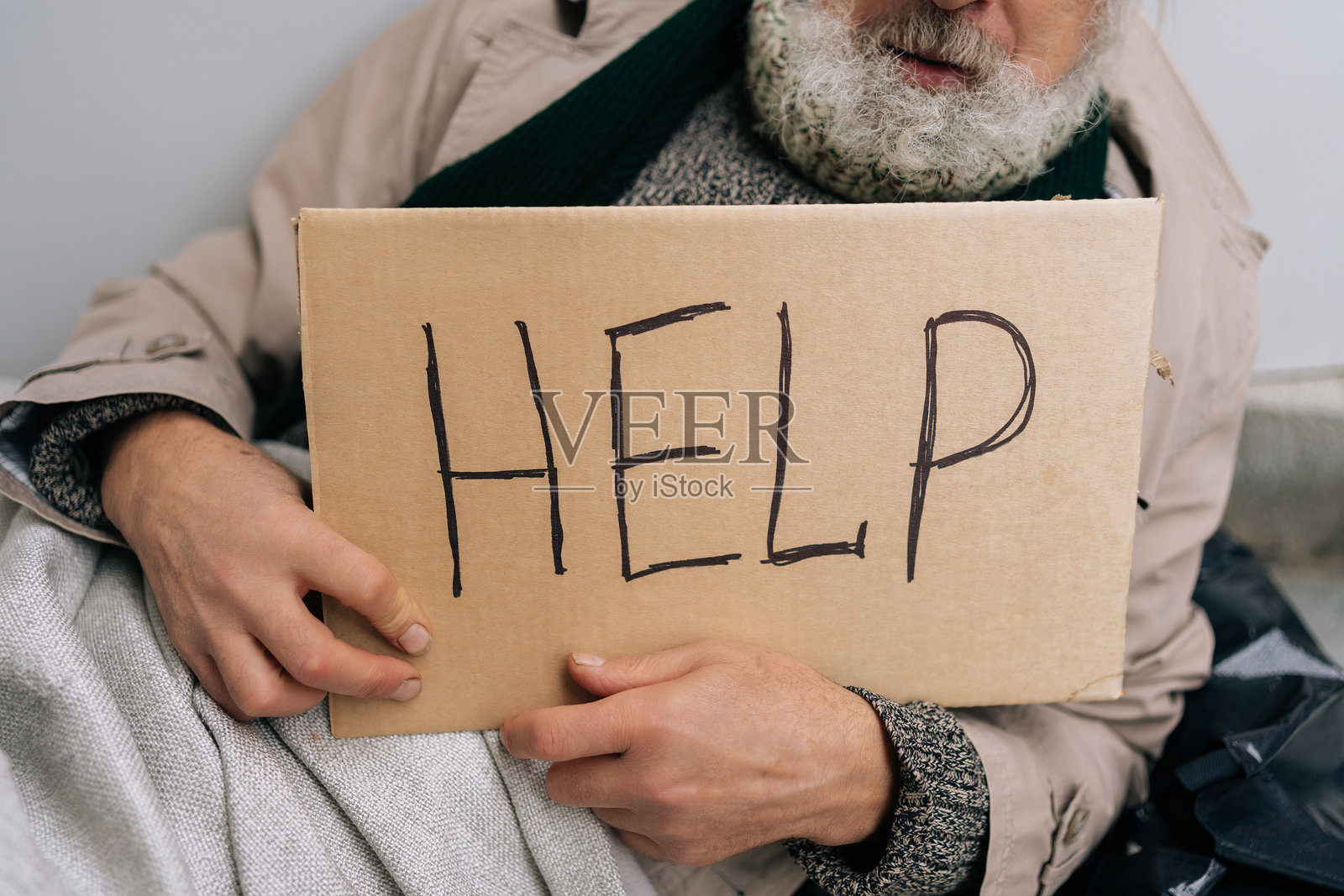 特写镜头，剪裁的画面显示一位不知名的年长无家可归者坐在寒冷的城市人行道上，手持求助的标志。贫困与脆弱的概念。照片摄影图片