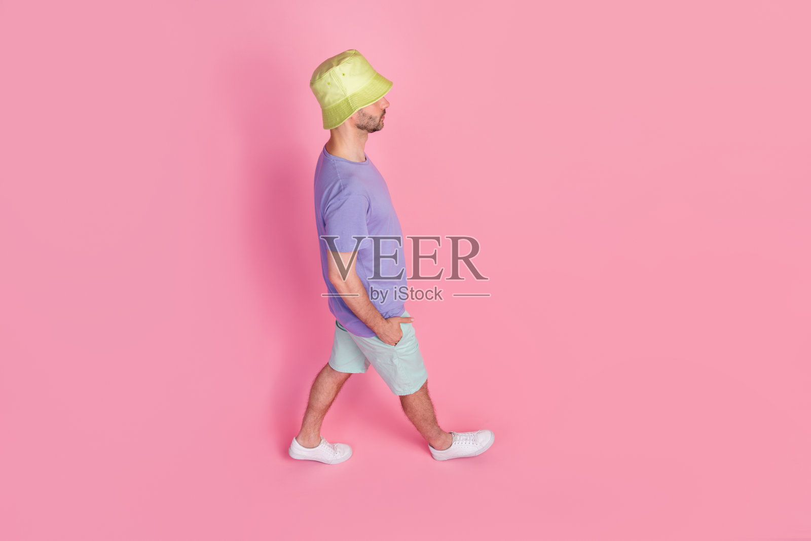 全身照片，高角度侧面视图，年轻男子穿着时尚的蓝色休闲装，走在粉色背景上，适合周末旅游。照片摄影图片