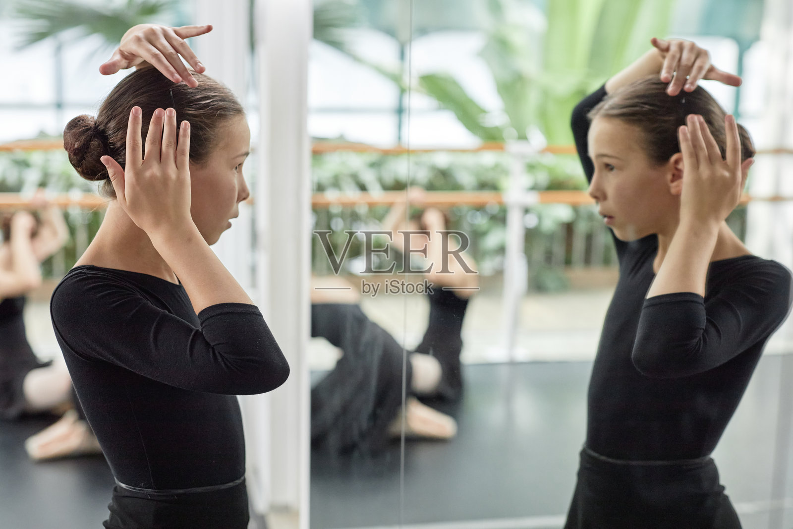 女芭蕾舞者在舞蹈室里用发夹整理发型，镜子前专注地打量自己。照片摄影图片