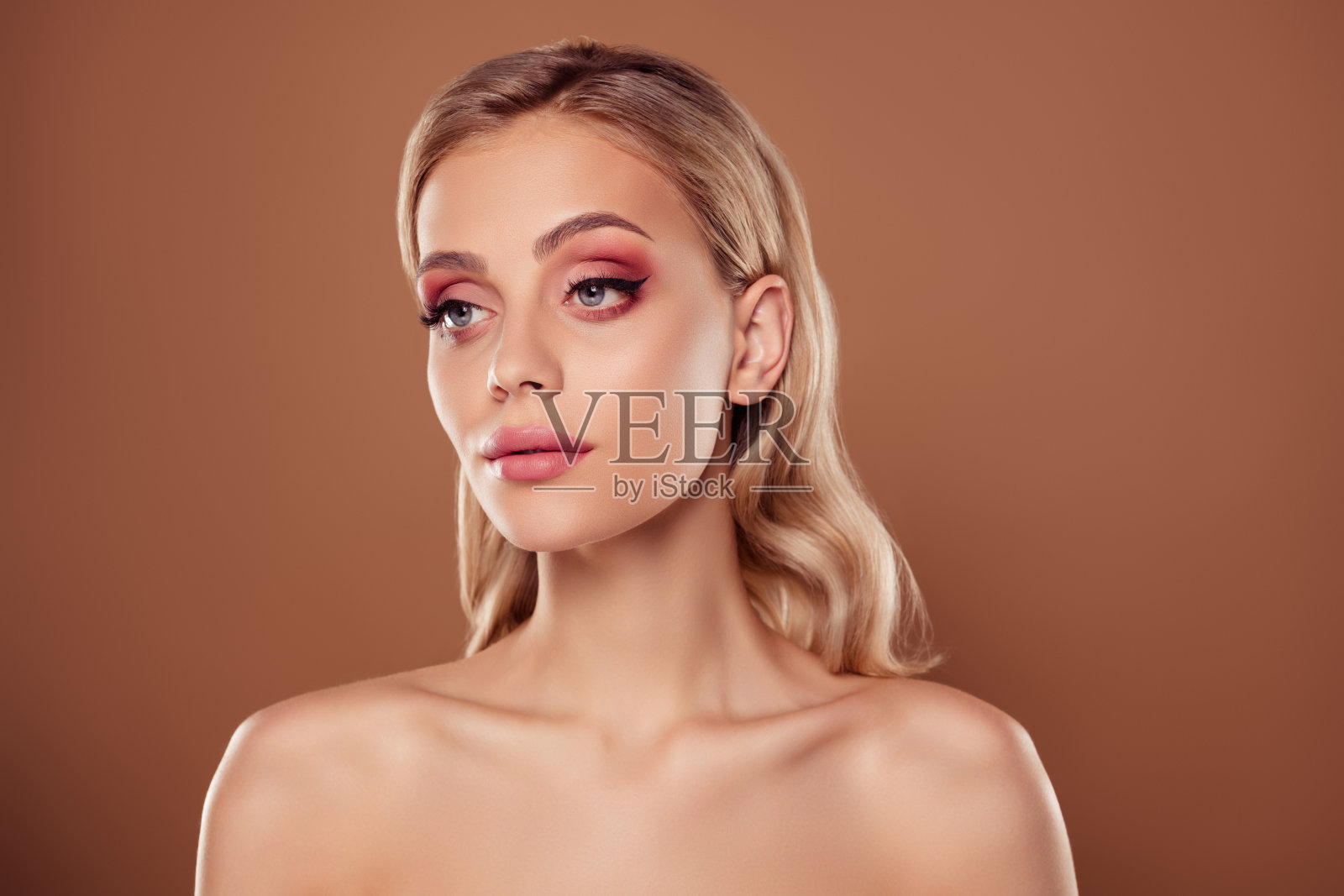 女孩侧面照，粉色妆容，背景为柔和的棕色。照片摄影图片