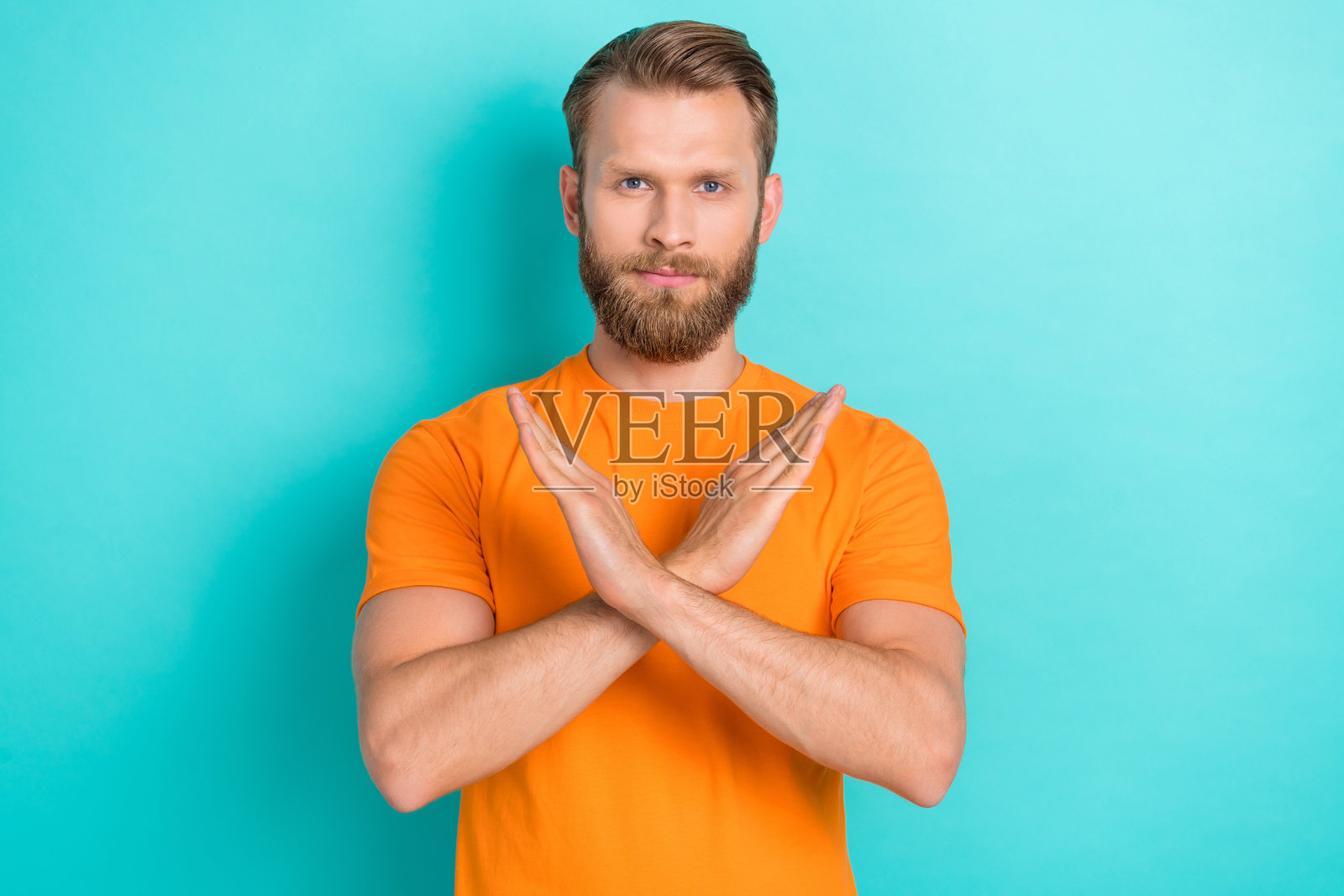 穿着橙色T恤、双臂交叉的严肃胡子男士，背景为青绿色。照片摄影图片