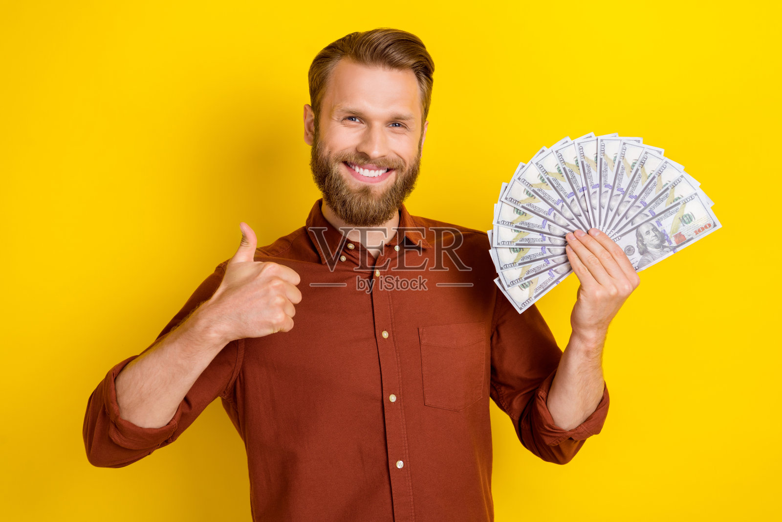 快乐友好的男人手持现金，竖起大拇指表示赞同，背景为黄色。照片摄影图片