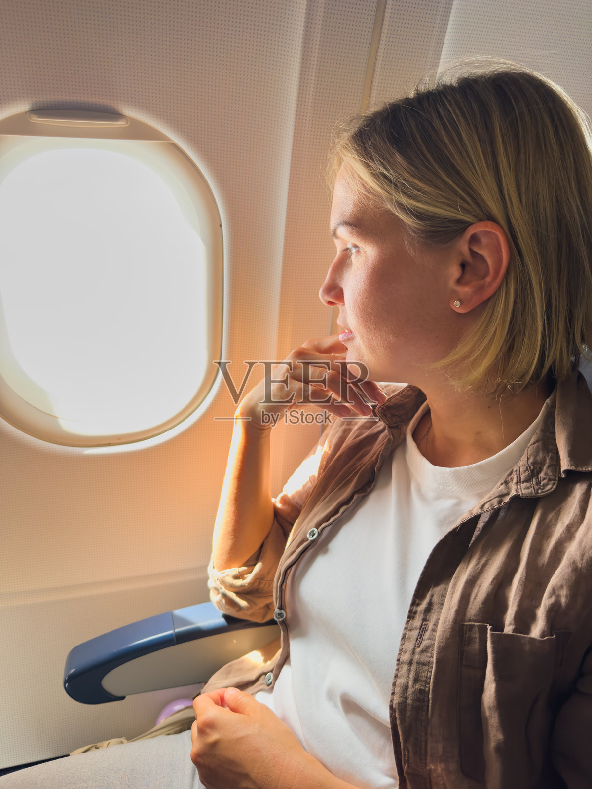 乘客女性在飞机上飞行。女孩坐在飞机上，透过窗户看外面，正在进行旅行度假。旅行中的女性在飞机内享受飞行。旅行的女孩。照片摄影图片