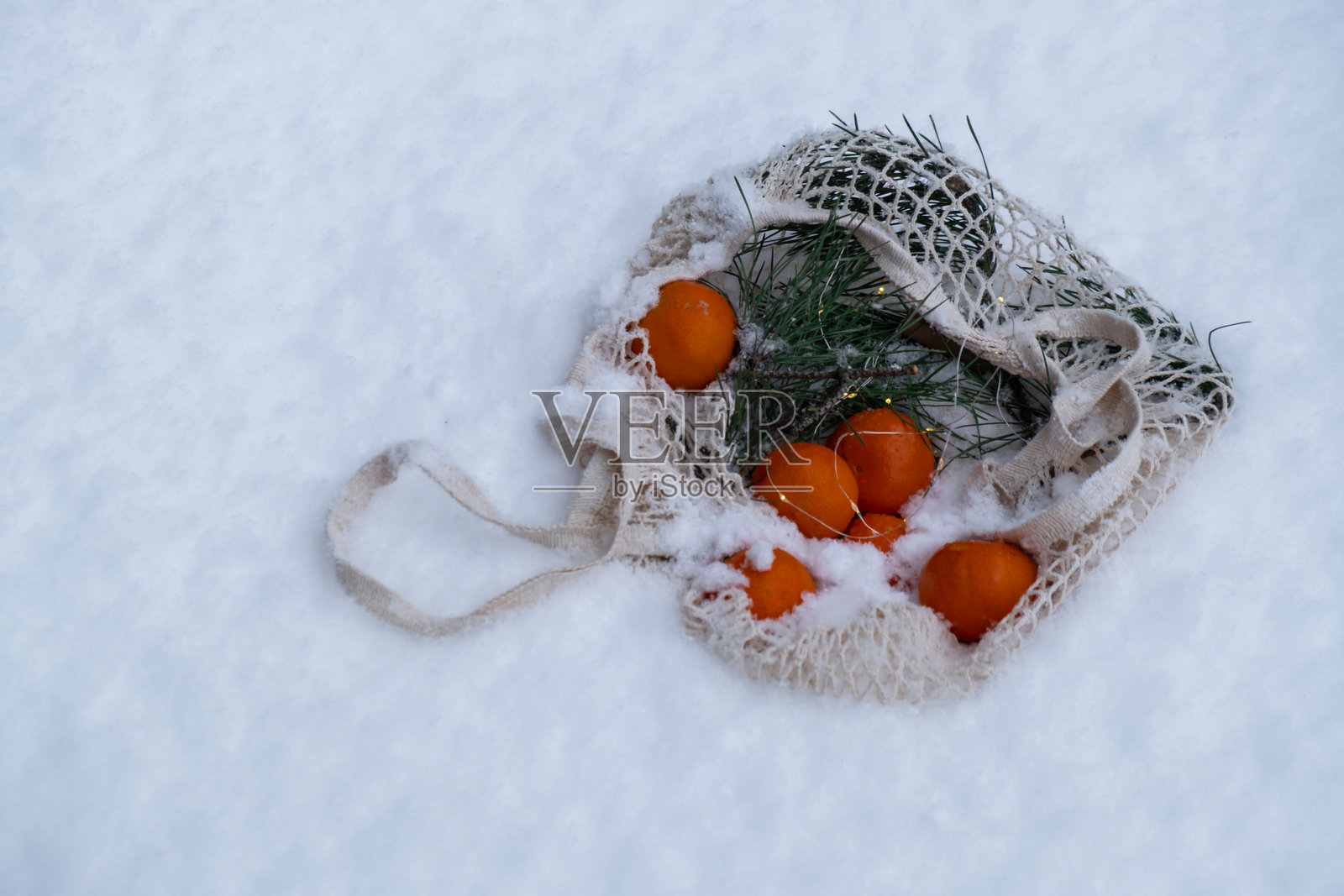 雪地户外的网状购物袋里装着橘子。绿色环保可持续的圣诞节理念。平铺在雪地背景上。负责任的选择。照片摄影图片