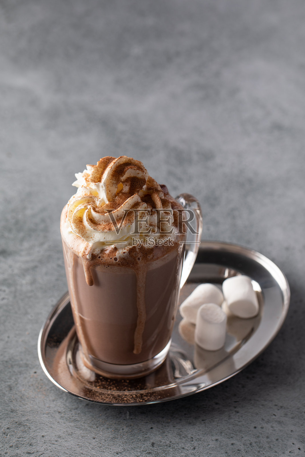 一杯丰富的热巧克力，上面装饰着奶油和肉桂，配有棉花糖，放在银色托盘上。照片摄影图片