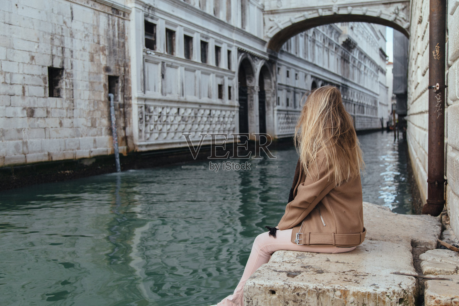 年轻女性坐在城市运河旁的侧面视图照片摄影图片