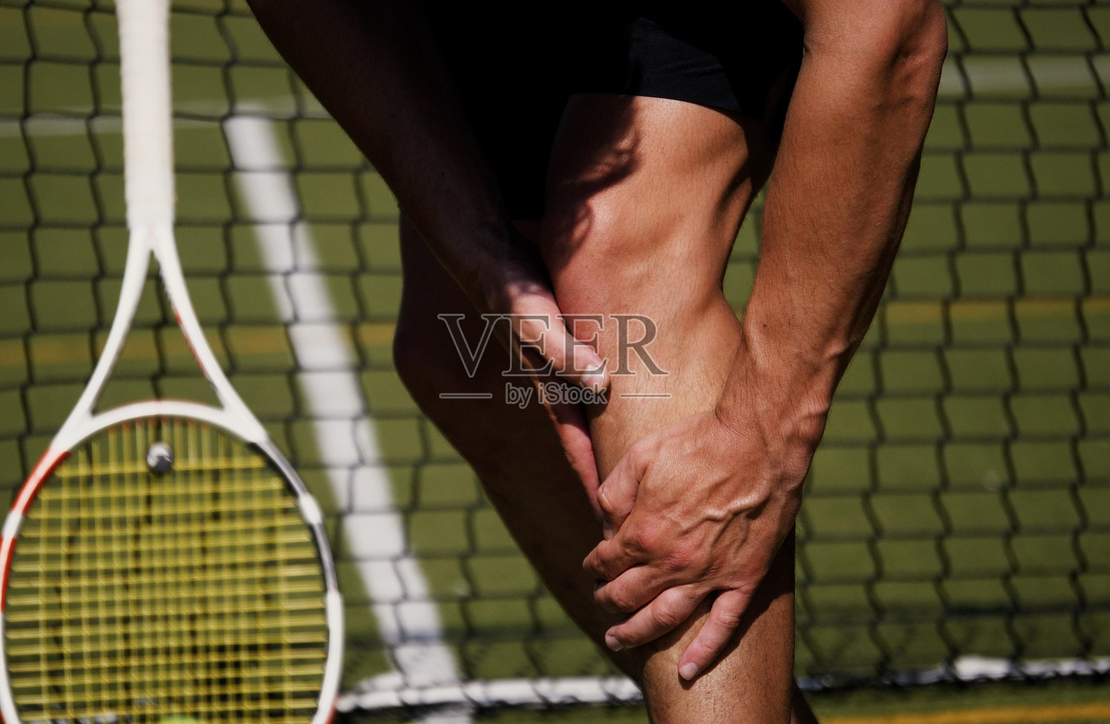 一名年轻男子在球场上打网球时膝盖受伤。照片摄影图片