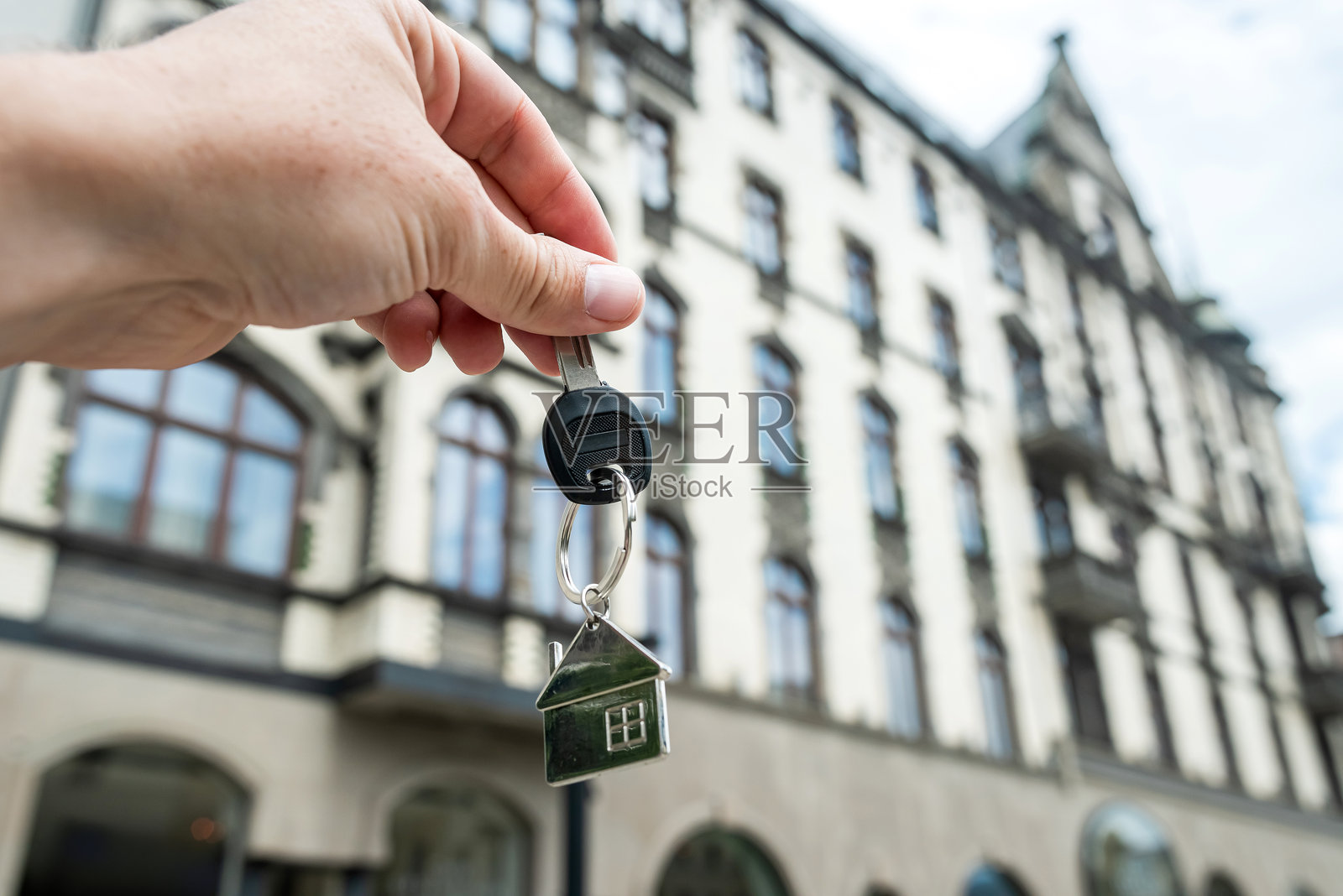 手拿钥匙从一个新的公寓对着现代化的办公中心。新公寓的房地产概念照片摄影图片