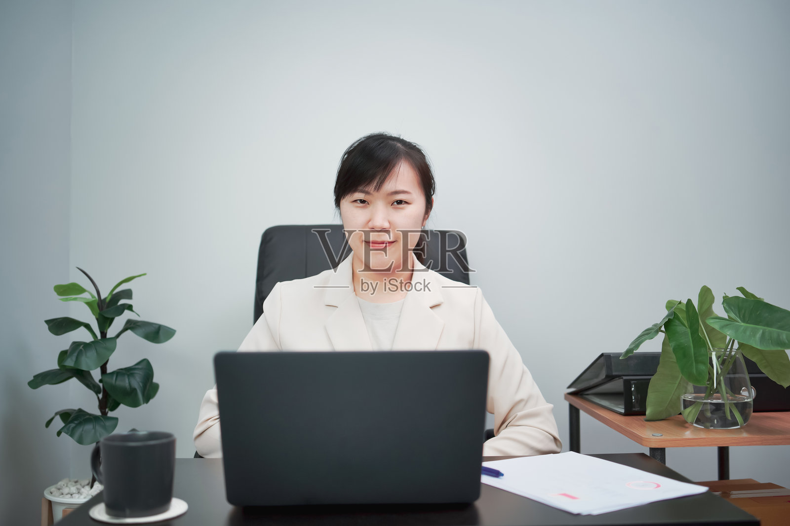 女性在笔记本电脑上打字，同时检查纸上的工作。照片摄影图片