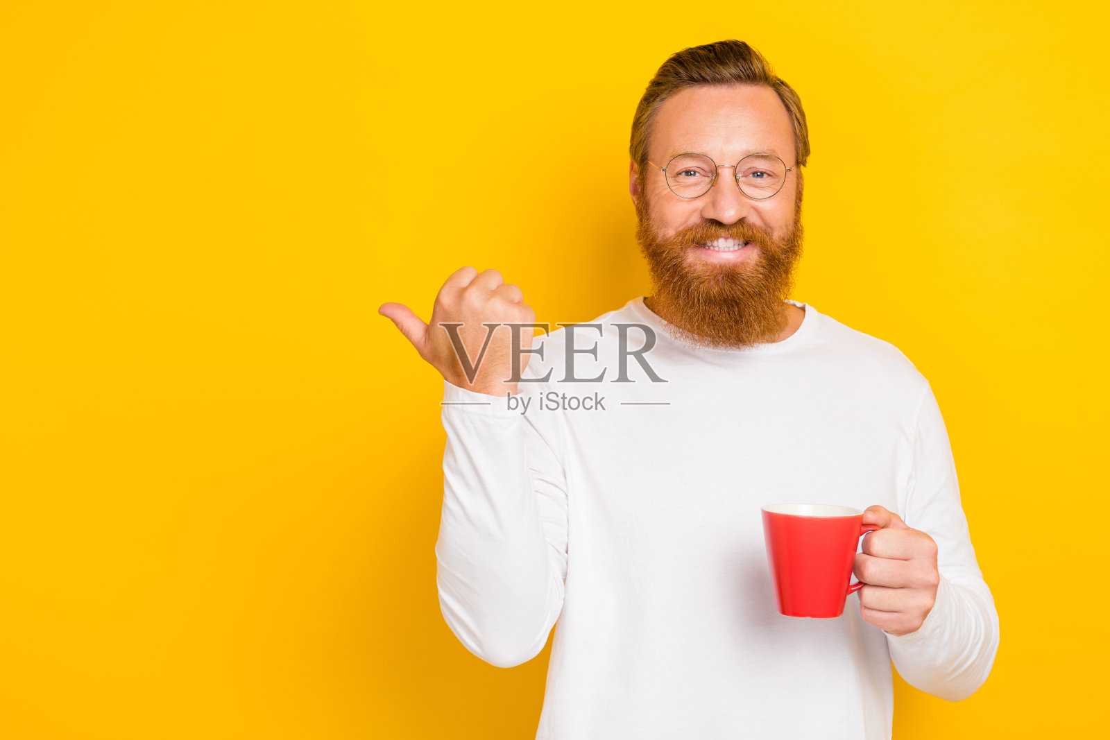 穿着时尚白色毛衣的积极男性，手持饮料，手臂伸出，面向空旷的空间，提供建议，背景为黄色。照片摄影图片