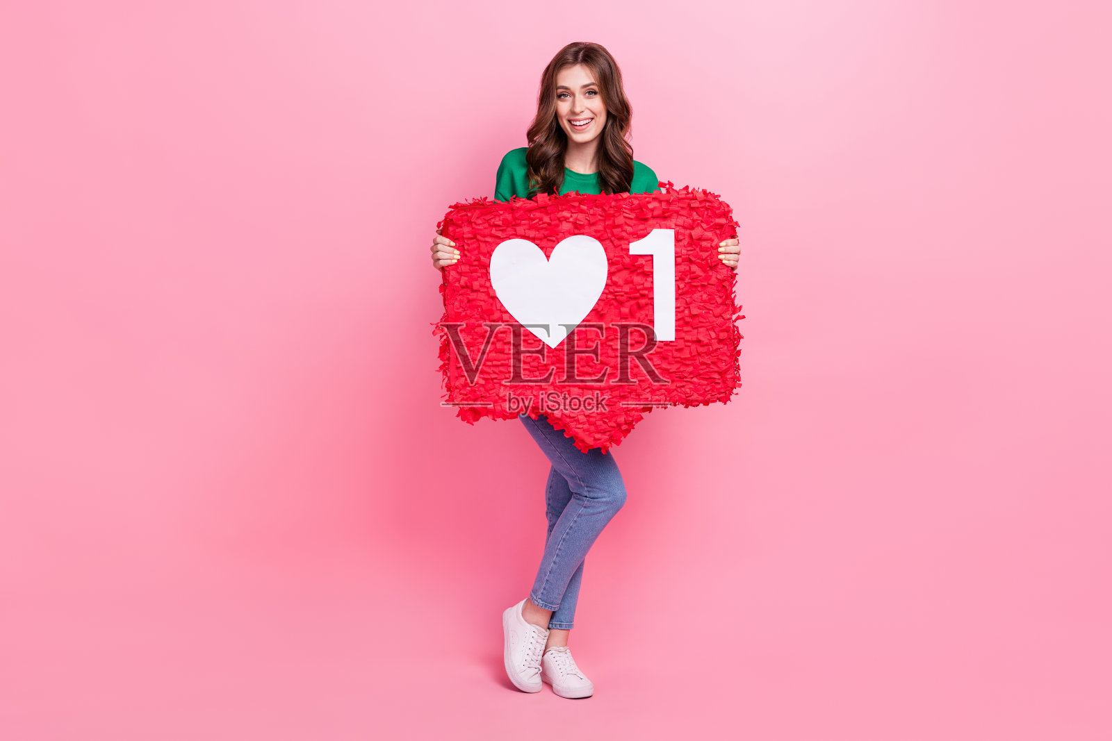 全身照的积极女性博主手持大纸卡，满意地展示粉丝活动，背景为粉色。照片摄影图片