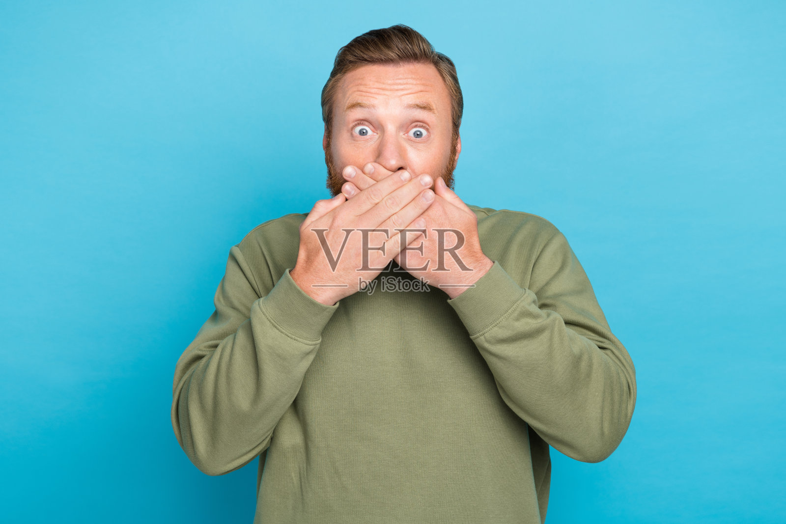 吸引人的年轻男子的照片肖像，惊恐地用手掌捂住嘴，穿着时尚的卡其色服装，背景为水绿色。照片摄影图片